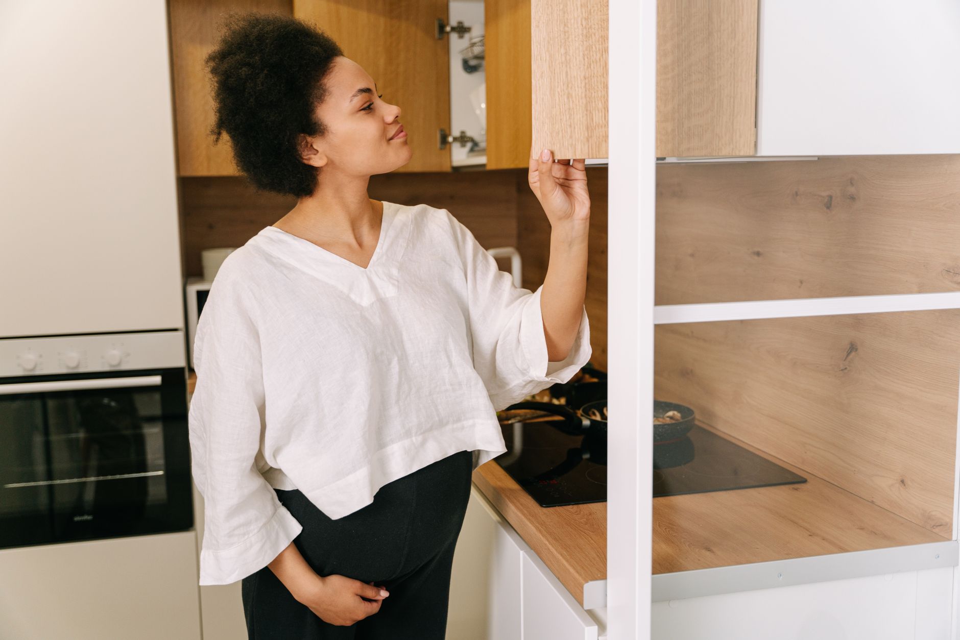 Pregnant woman using a supportive maternity belt while standing in a kitchen, natural light, soft pastel decor