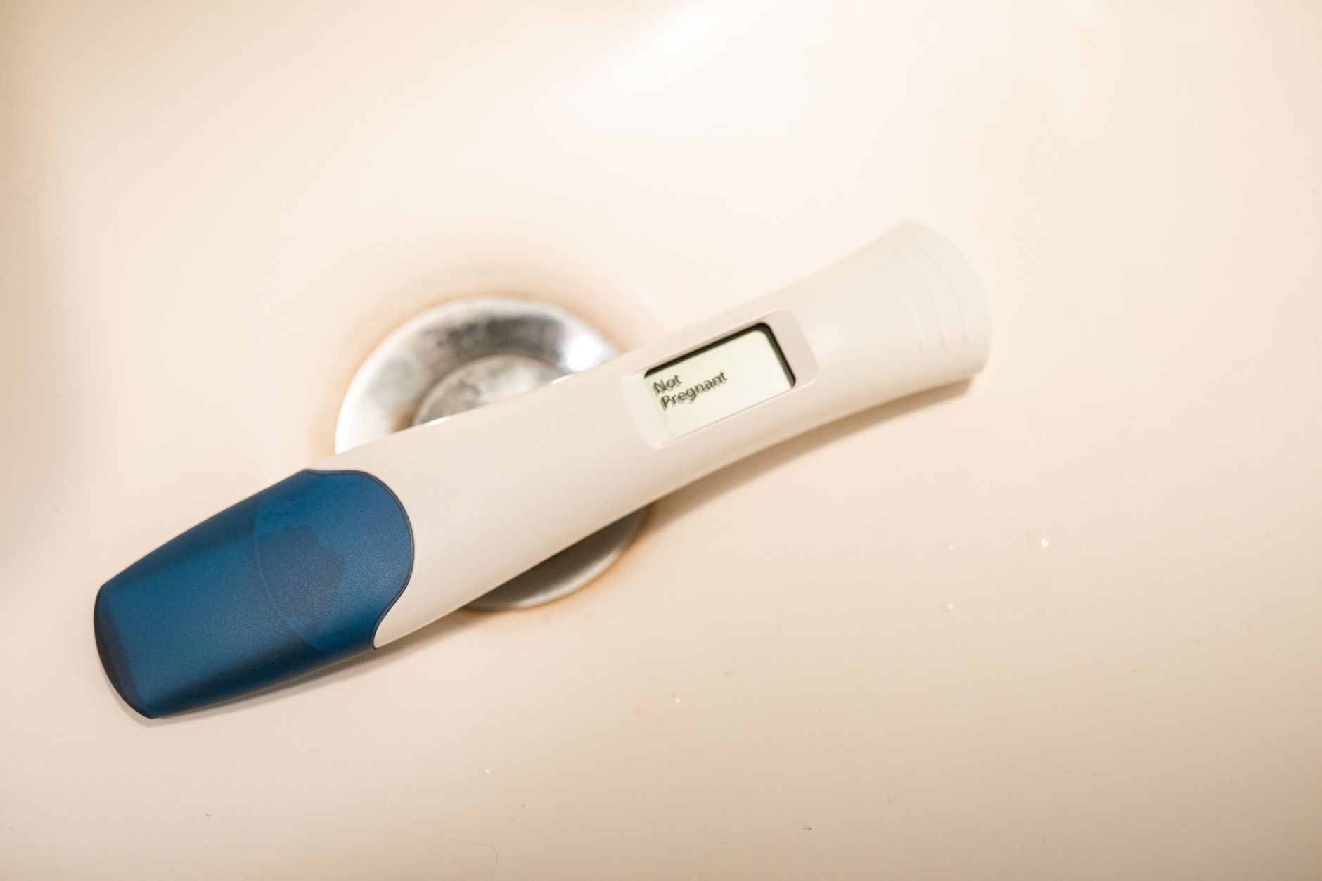 A bright kitchen counter with a digital pregnancy test displaying the word 'Pregnant' in green letters, next to a glass of water and a sunrise window