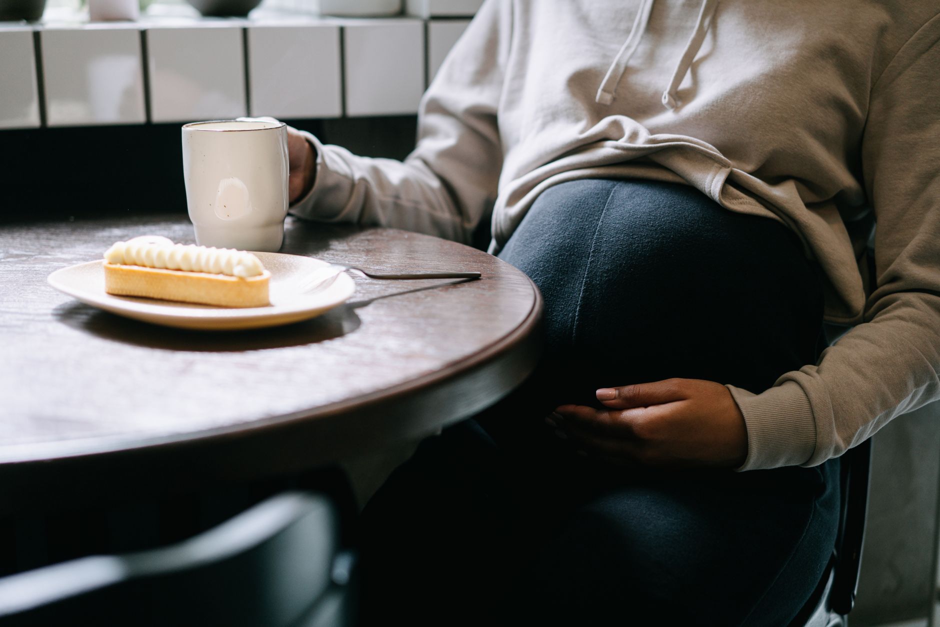 A pregnant woman sitting at a kitchen table, holding a glass of water and a small plate of Brazil nuts, soft natural light, cozy home setting