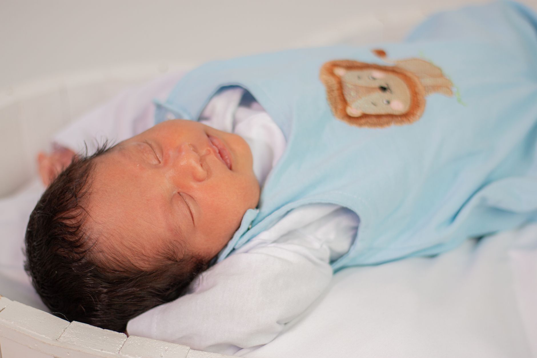 A newborn swaddled in a soft blanket, lying in a semi‑prone position on a wooden nursery table, natural morning light