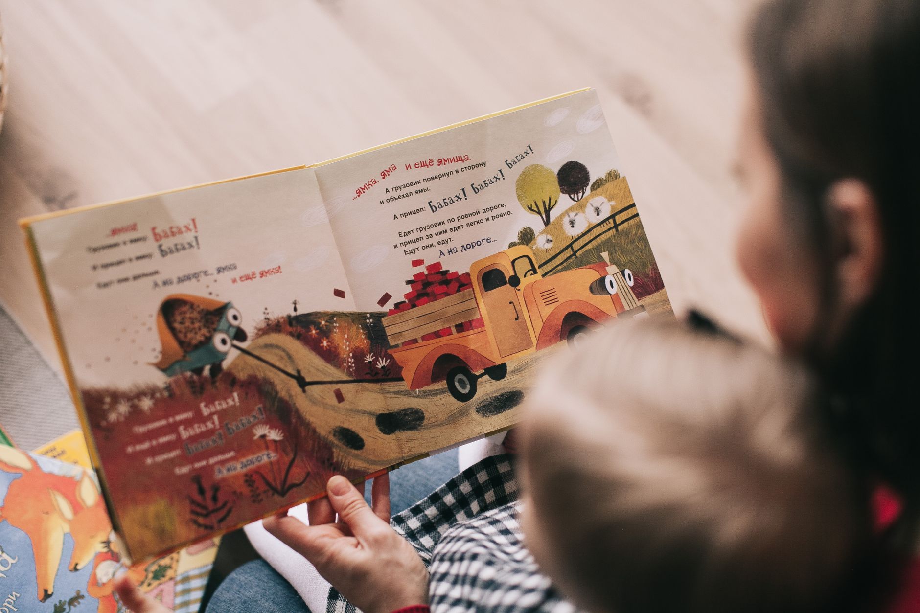 A mom and her child sitting together on a rug, each reading their own book, demonstrating parallel reading time.