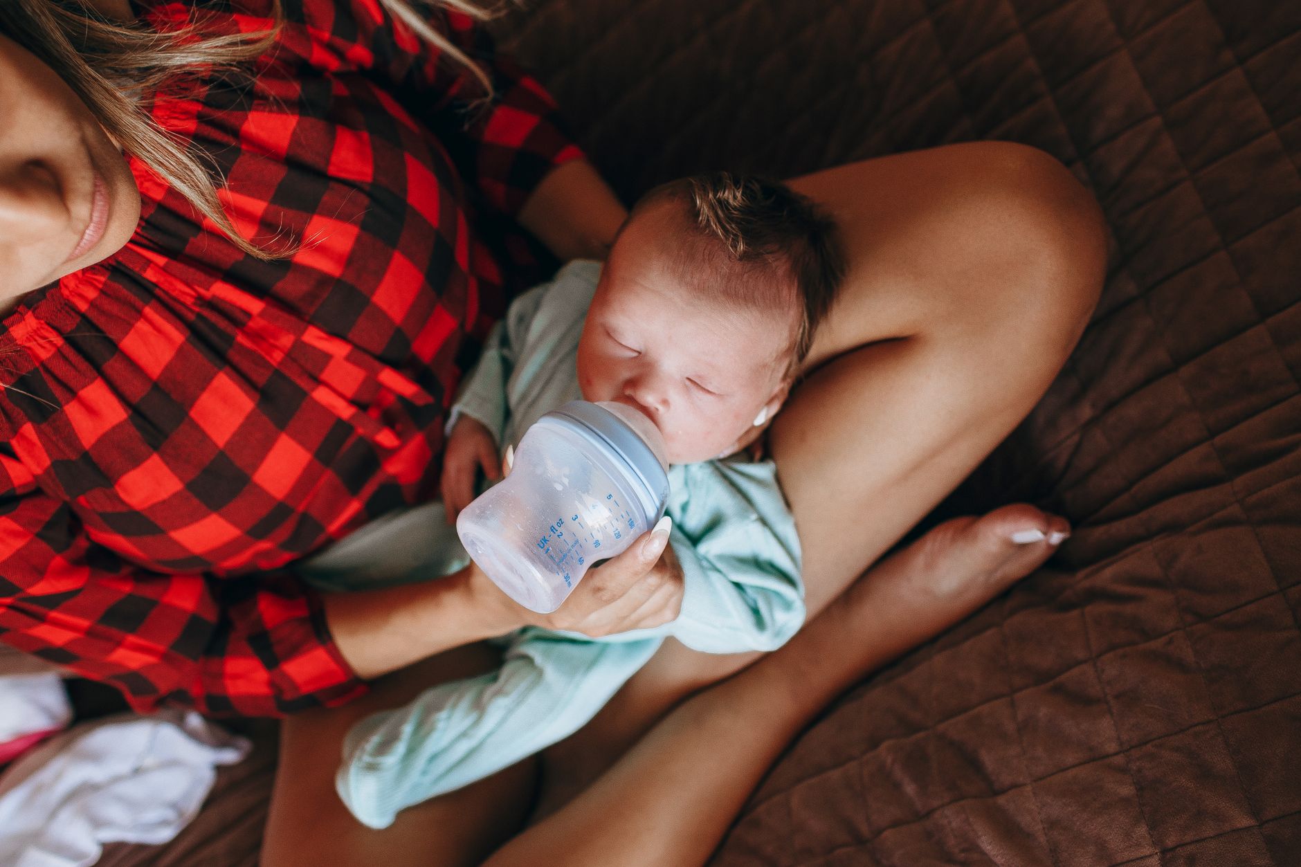 Mother gently feeding a newborn in a bright kitchen, sunlit window, soft pastel colors