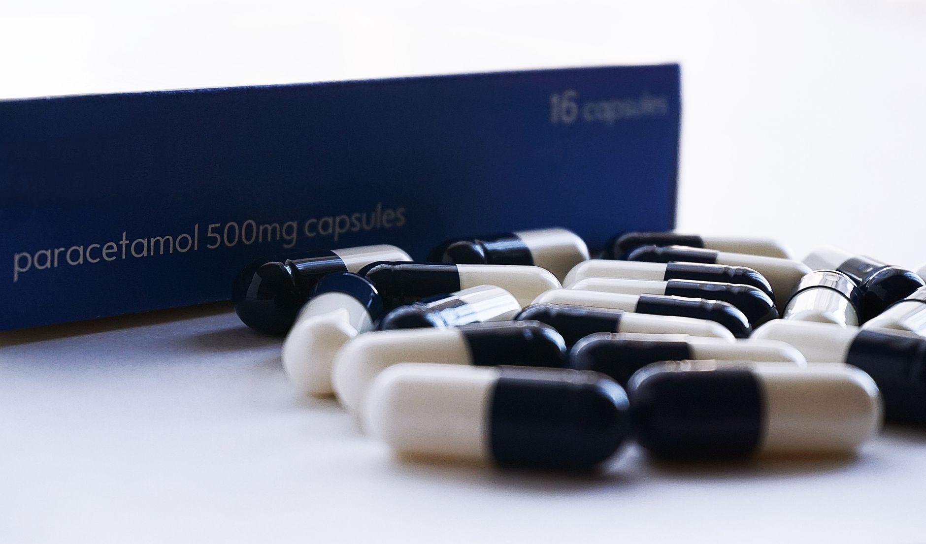 A variety of over-the-counter medication bottles and boxes on a clean white shelf, with a focus on acetaminophen brands.