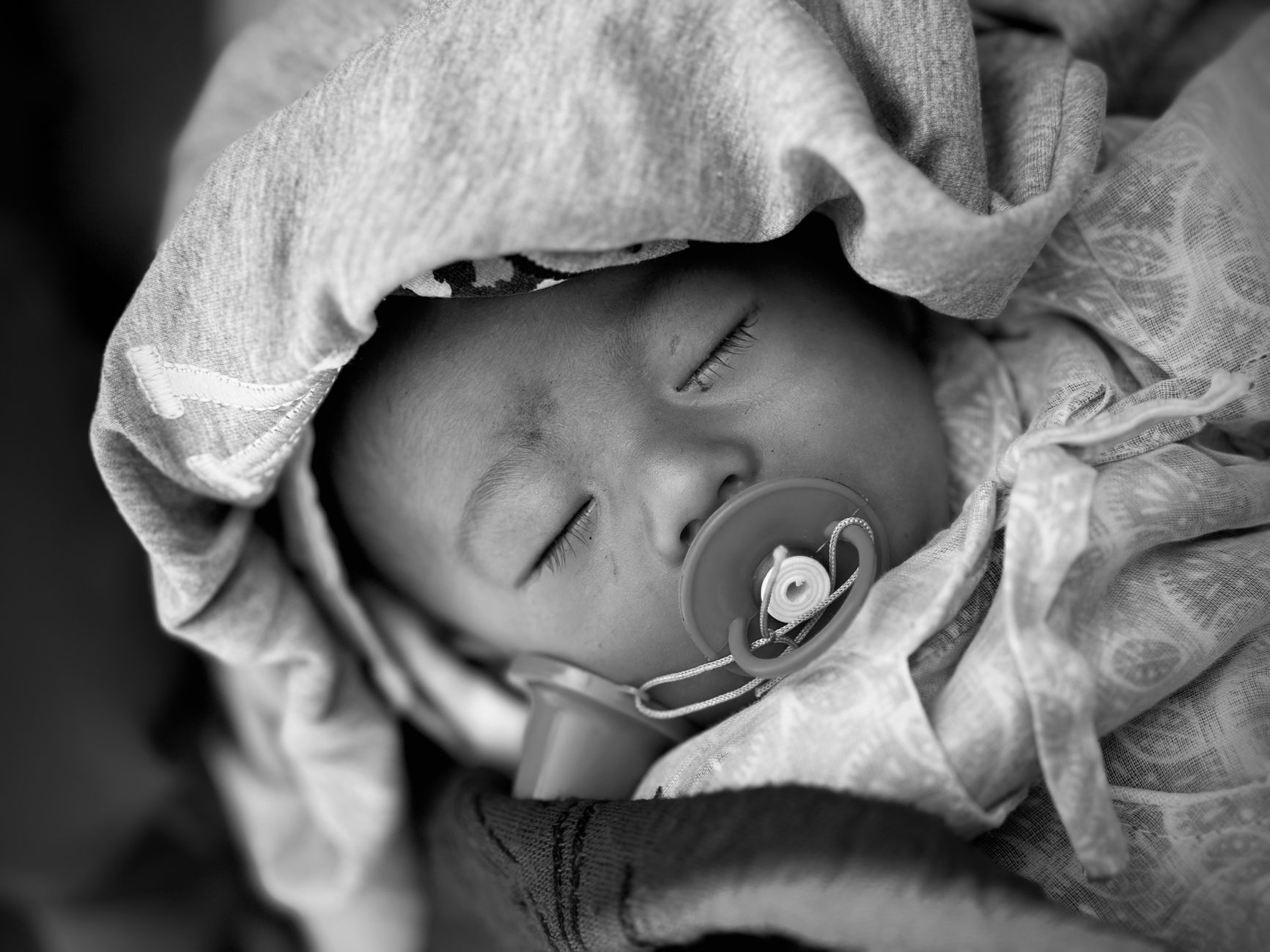 A soft, breathable sleep sack laid next to a newborn in a crib, with a pacifier nearby, highlighting safe sleep essentials