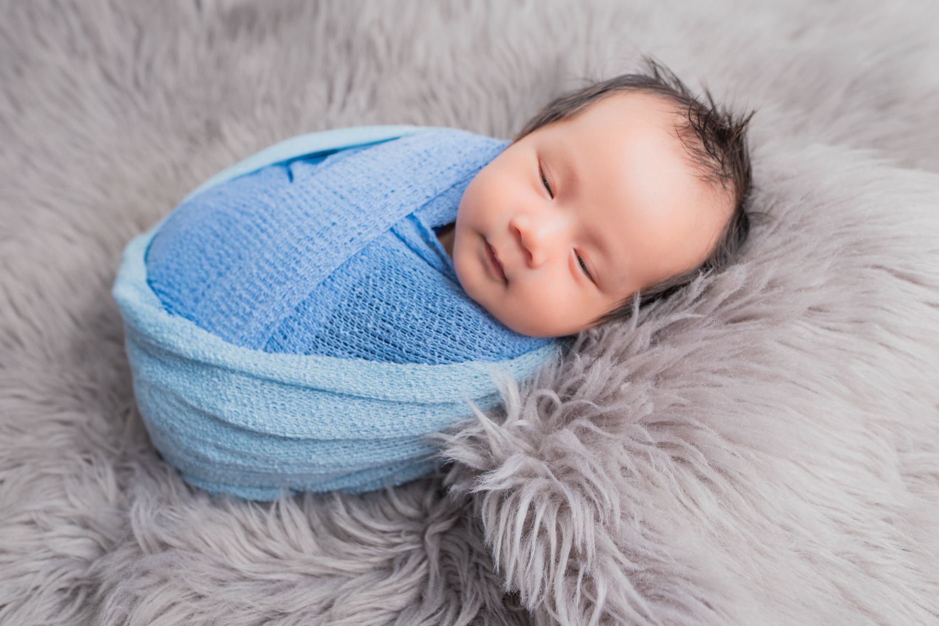 Close‑up of a newborn sleeping peacefully on its back in a breathable sleep sack, with a rolled towel supporting the side for extra safety