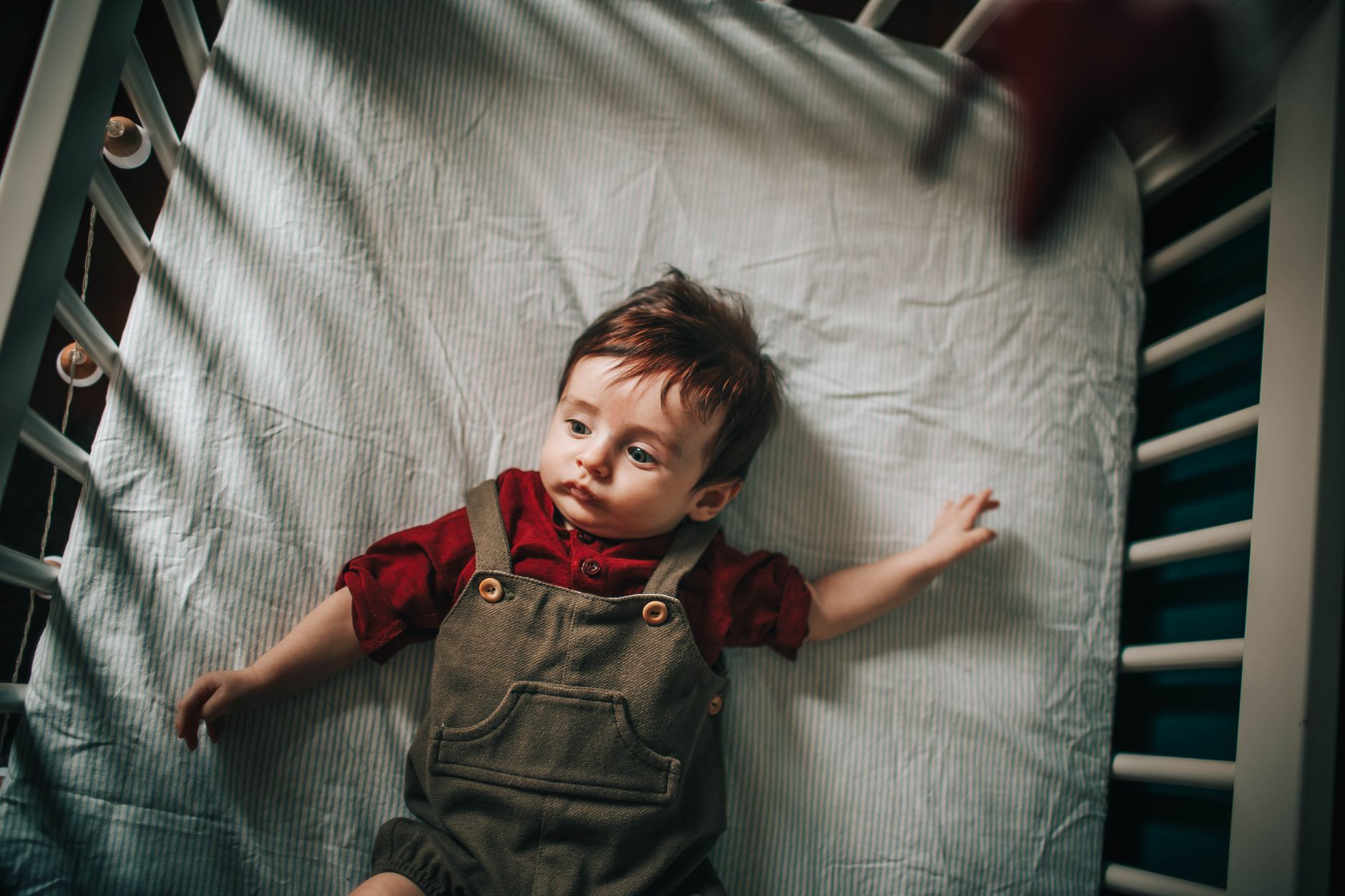 A baby sleeping peacefully on their back in a firm crib with a breathable swaddle sack, soft natural light streaming in