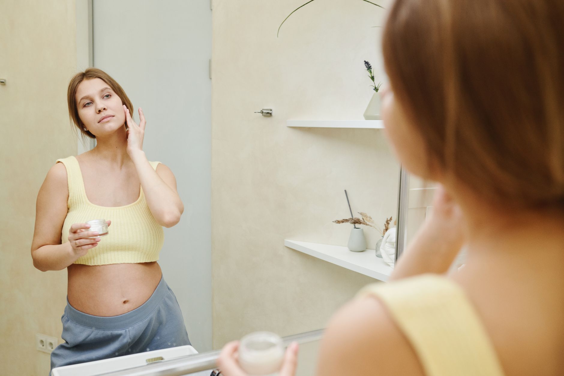 Pregnant woman in loose clothing looking at her reflection.