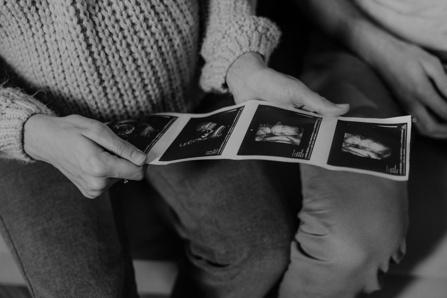 A mom sitting on a couch with her toddler, looking at an ultrasound photo together