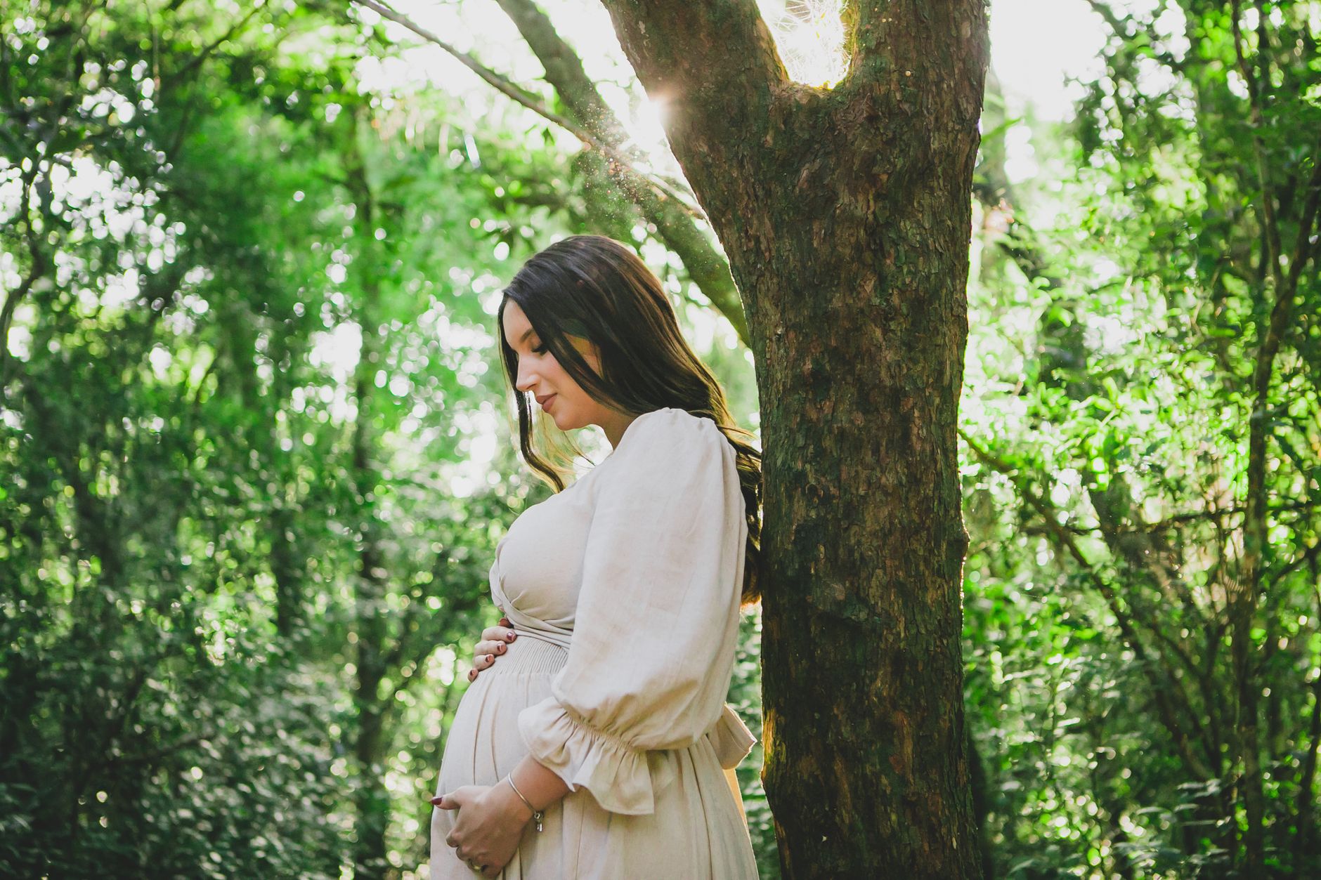 Pregnant woman walking on a sunlit park trail, wearing comfortable athletic wear, soft natural lighting, vibrant greenery surrounding the path
