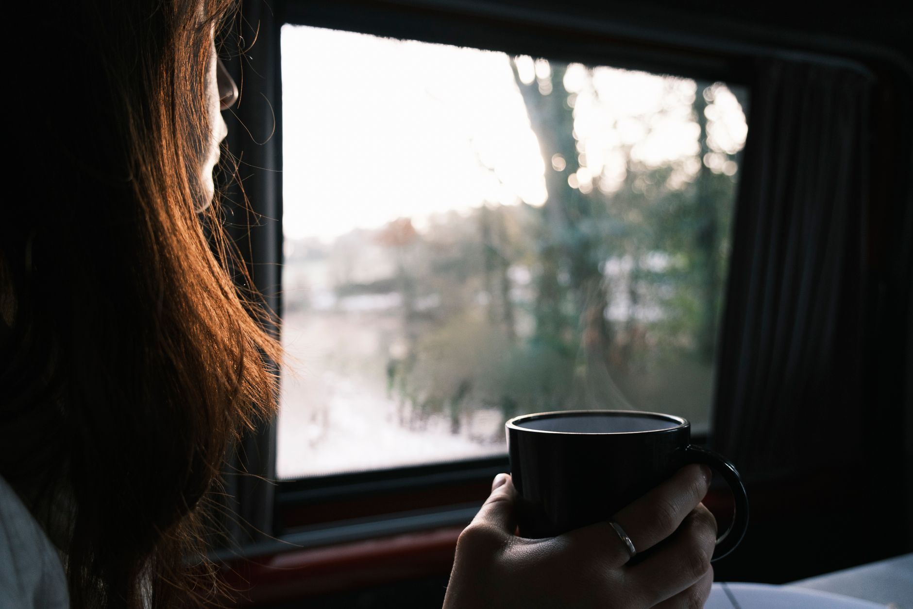 A mom sitting on a couch, looking out a window at a snowy landscape.