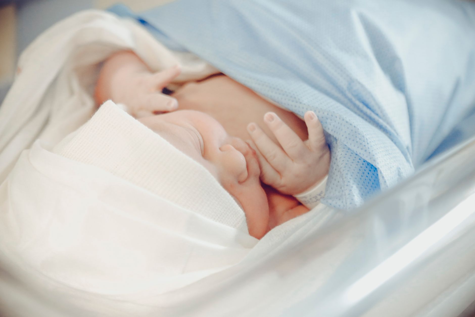 Infant lying under a phototherapy blanket, soft blue light glowing, mother watching from bedside