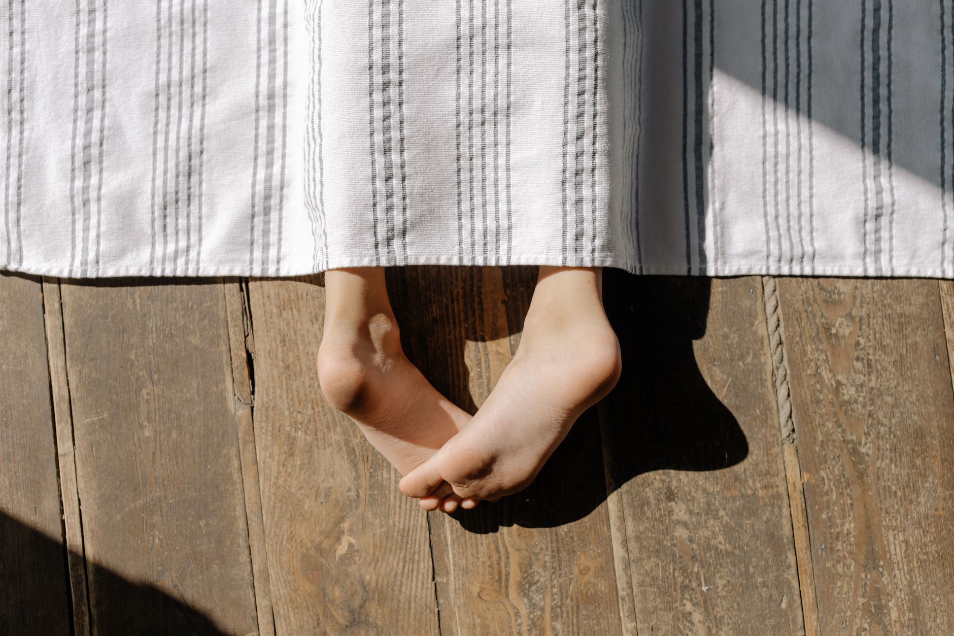Close‑up of a child’s feet standing on a ruler, bright morning light through a window, soft wooden floor