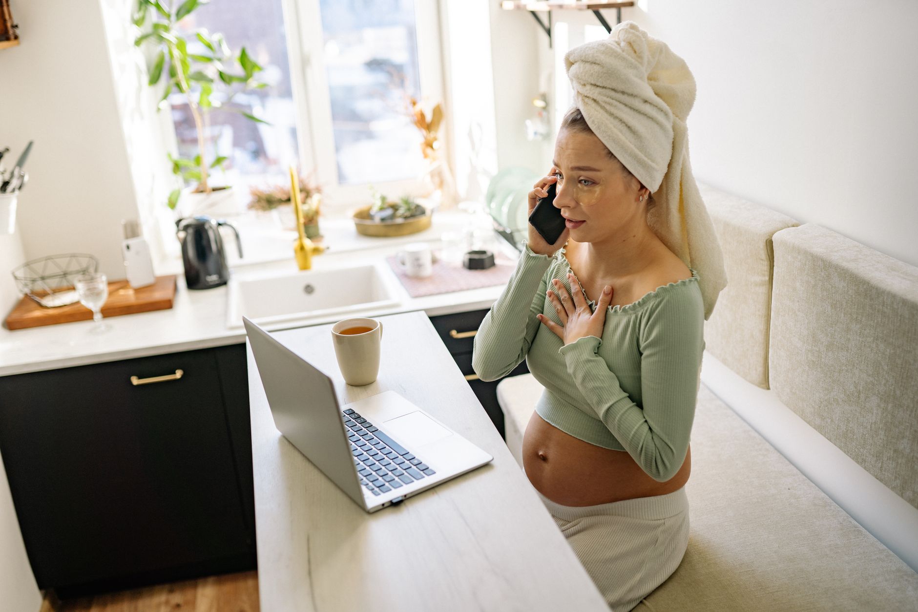 Pregnant person holding a prenatal care checklist, soft daylight on a wooden table with a cup of tea and a baby aspirin bottle