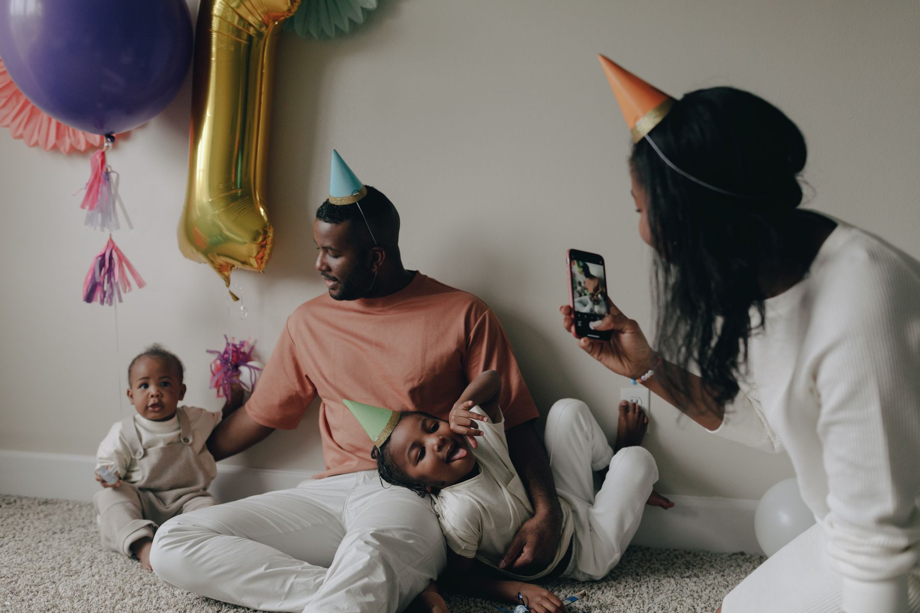A mom sitting on the floor with her two kids, one holding a coloring book and the other a science experiment kit, both smiling at the camera