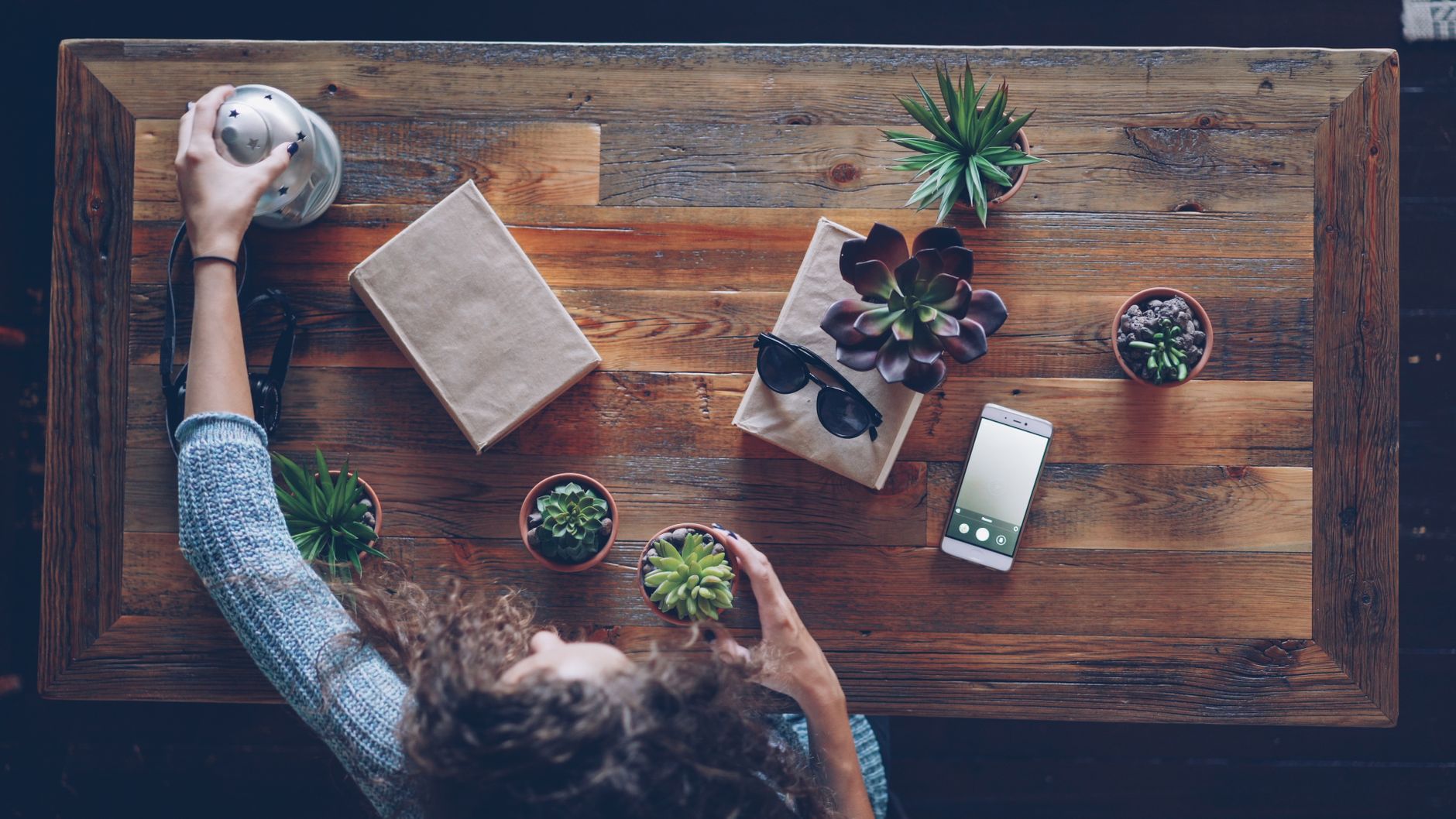 A hand‑held notebook with a pen, a small succulent plant, and a cup of tea on a light wood table, evoking calm and reflection
