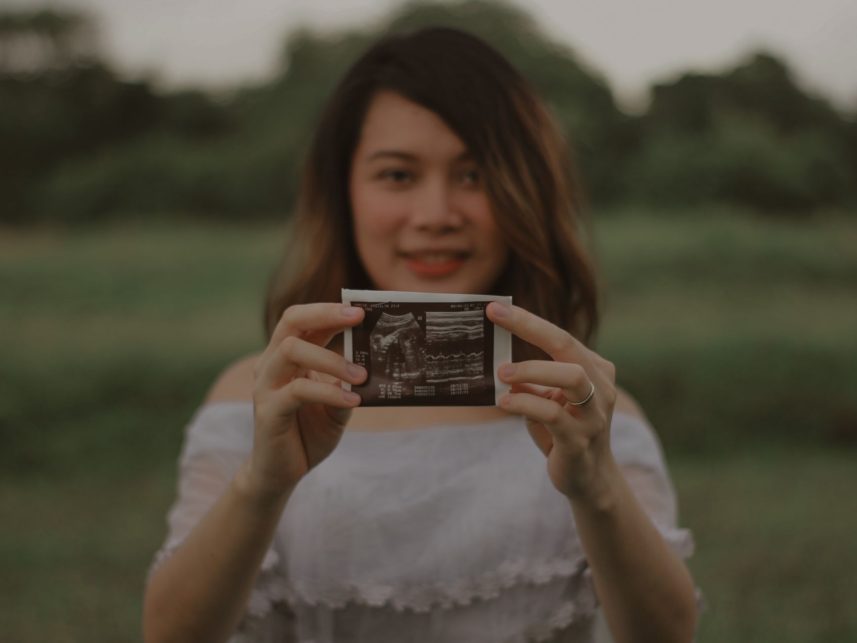 A woman in her 30s smiles at a framed ultrasound photo on her shelf, surrounded by books on parenting and family law