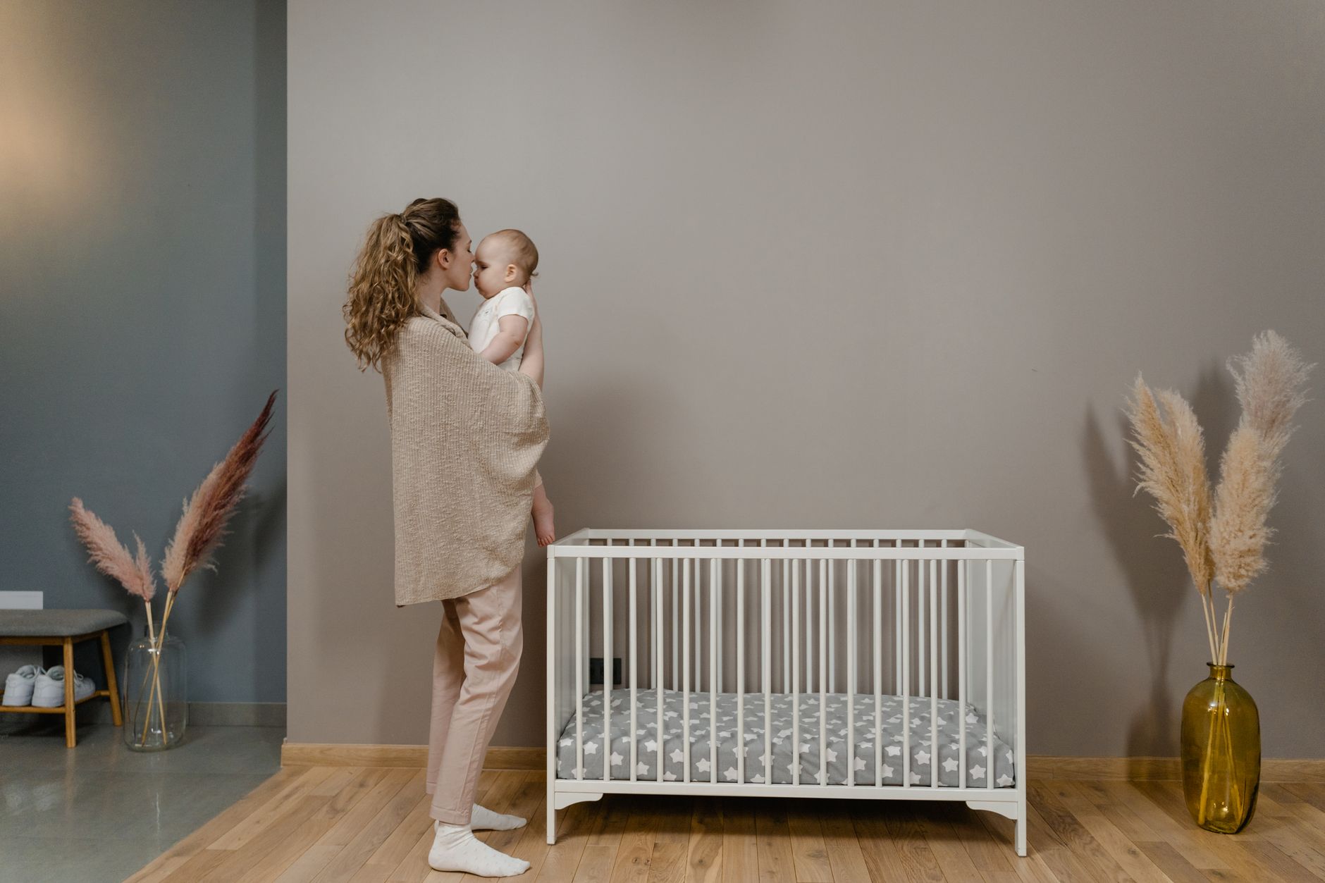 A mother gently comforting her 6-month-old baby in a crib during sleep training.