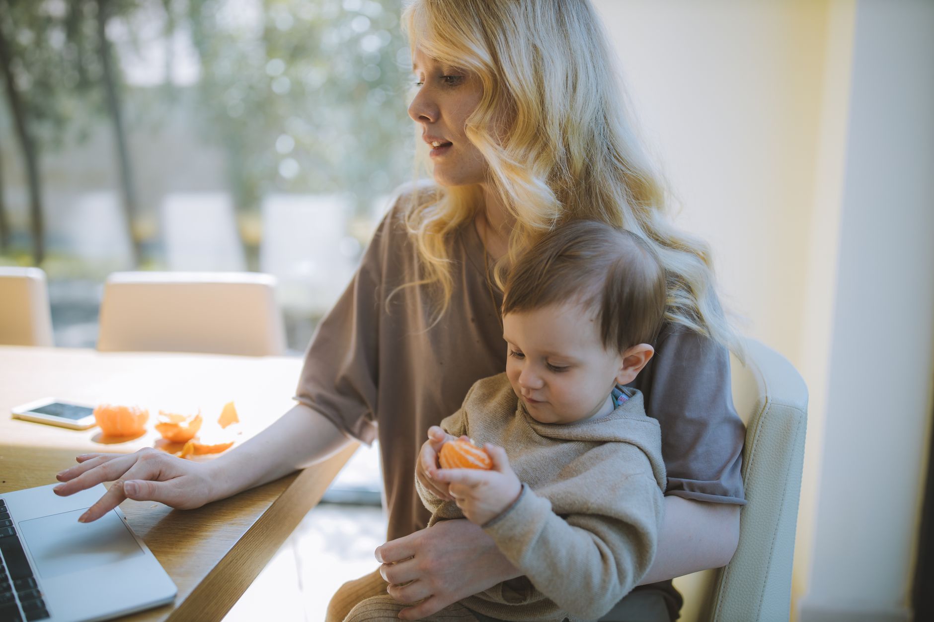 A mom working at a desk with her toddler playing nearby on a play mat