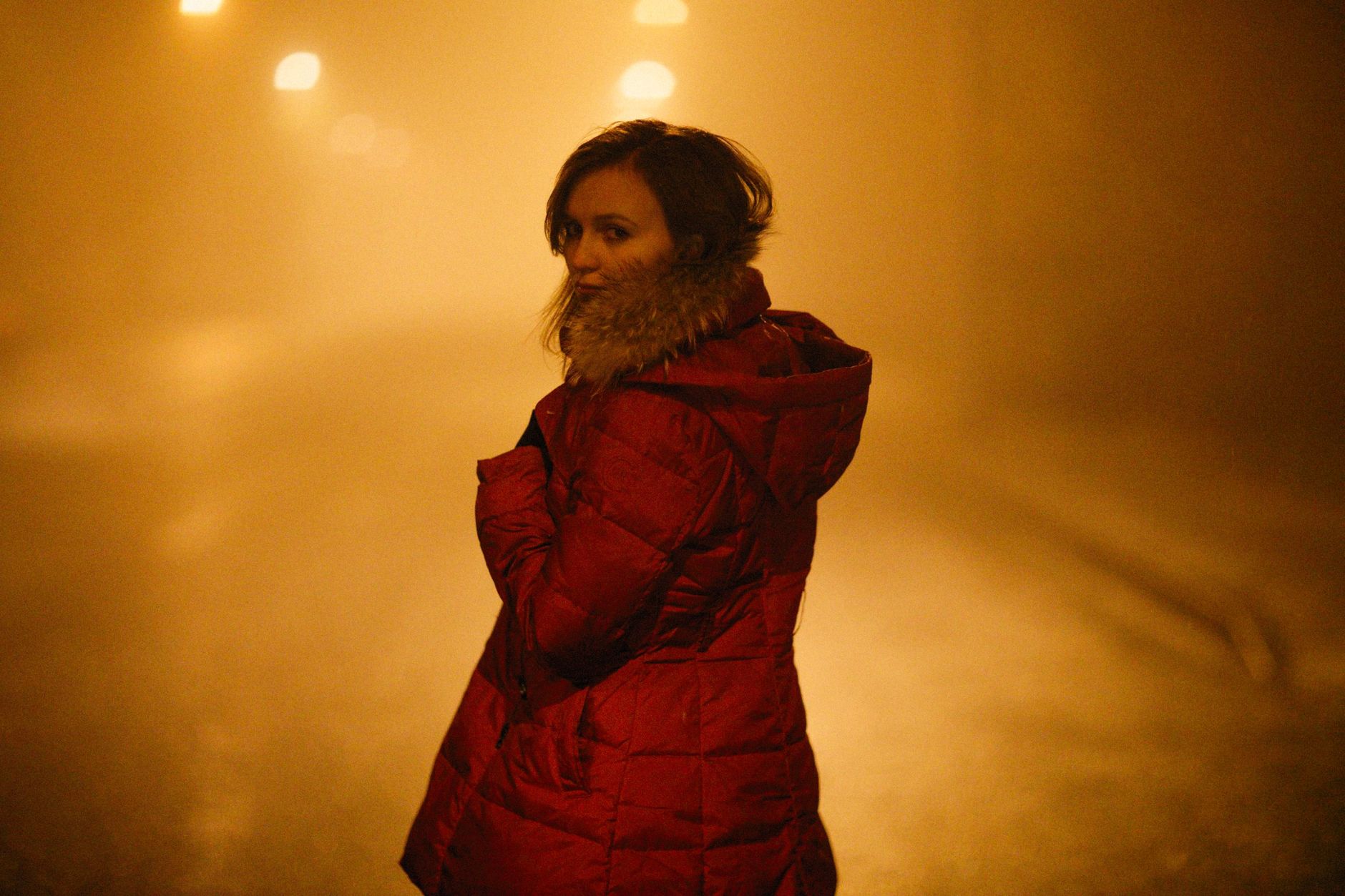 Mother holding a toddler on a stroller walk during a cool evening, with gentle streetlights and a light mist in the background