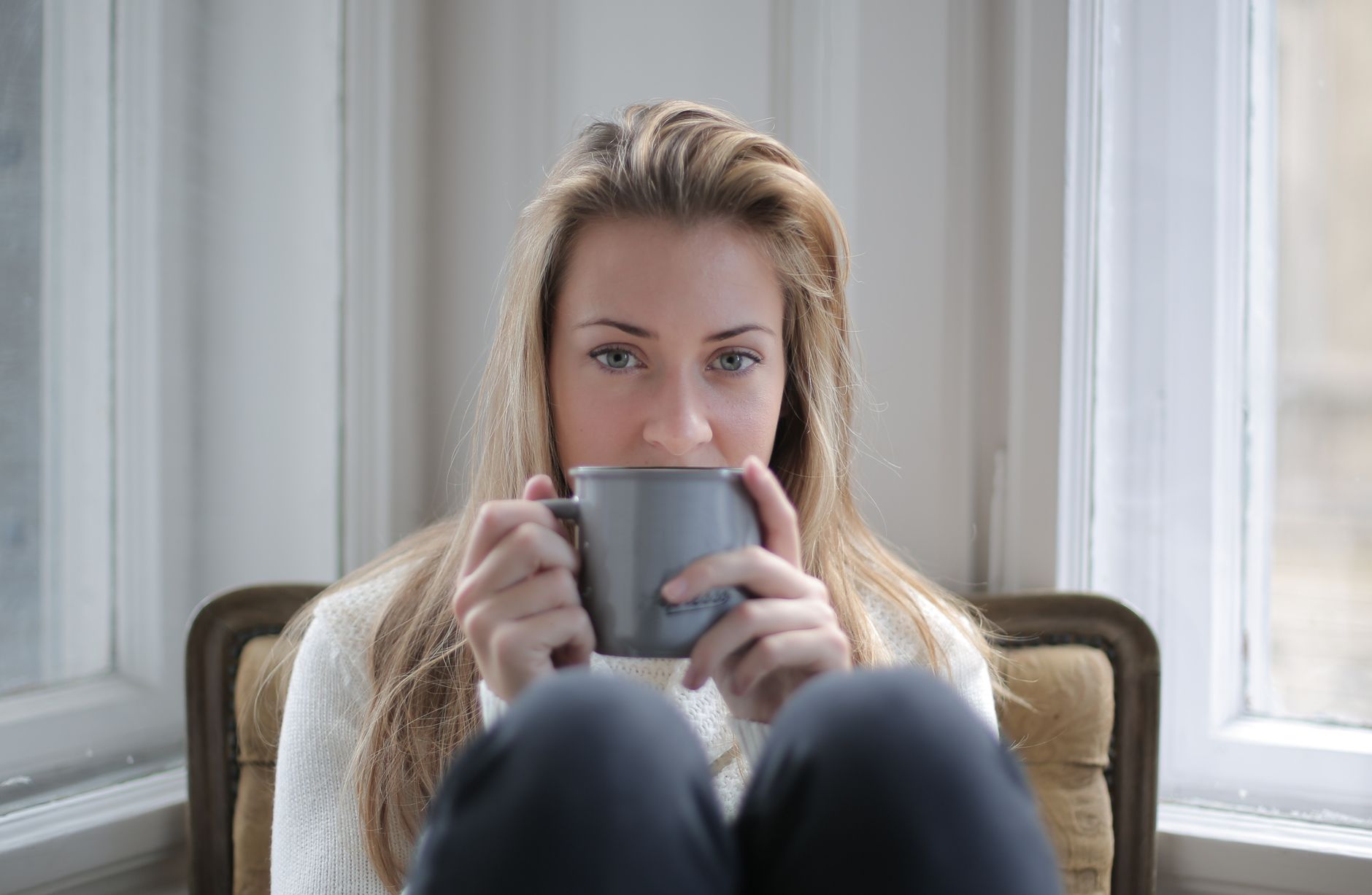 A soft-focus photograph of a pregnant woman resting on a couch with a blanket, a cup of herbal tea, and a small plate of fruit beside her