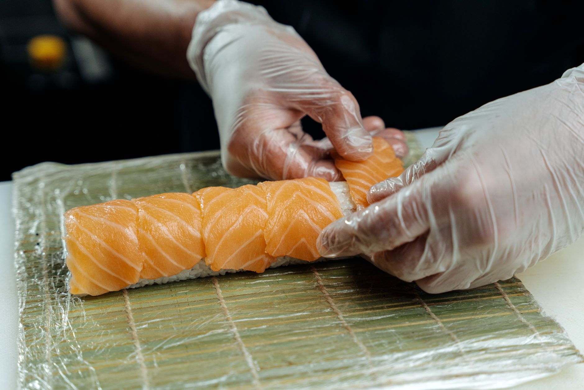 A cozy kitchen scene with a pregnant woman rolling sushi on a bamboo mat, fresh vegetables and cooked fish laid out on the counter, soft natural light