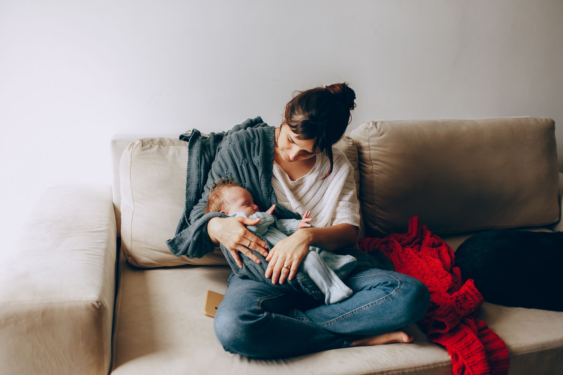 A mother sitting on a cozy couch, nursing her baby under a soft blanket, with a small handheld fan nearby