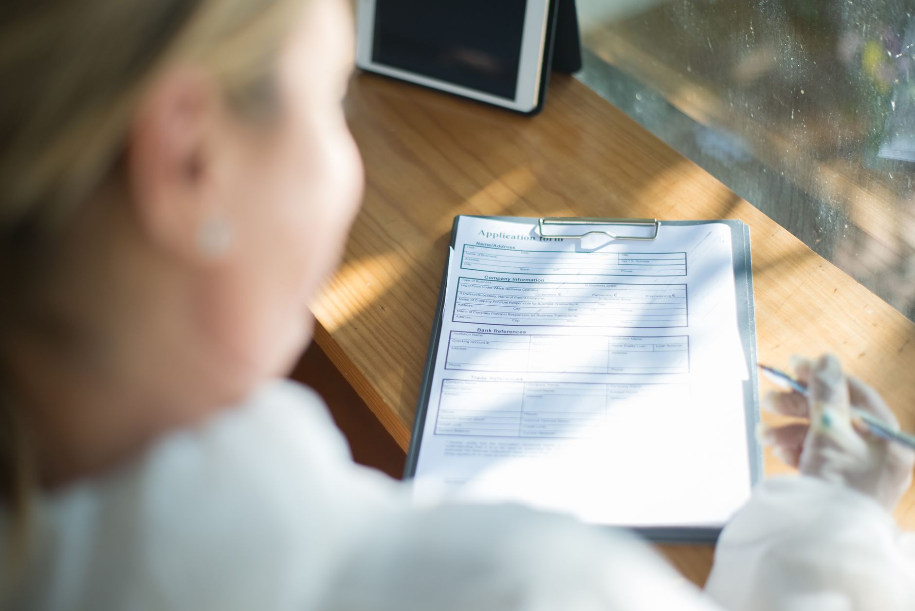 Woman's hands holding a tablet and a pen, focusing on an online application form, representing the ease of applying for no-medical-exam life insurance.