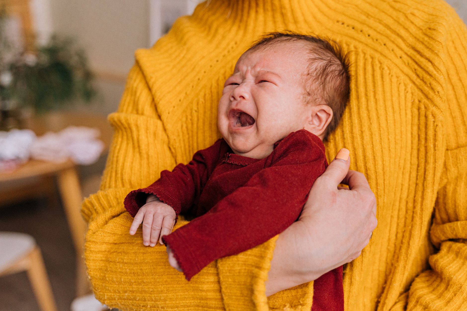 A close-up of a newborn baby crying, with a concerned mom holding them gently