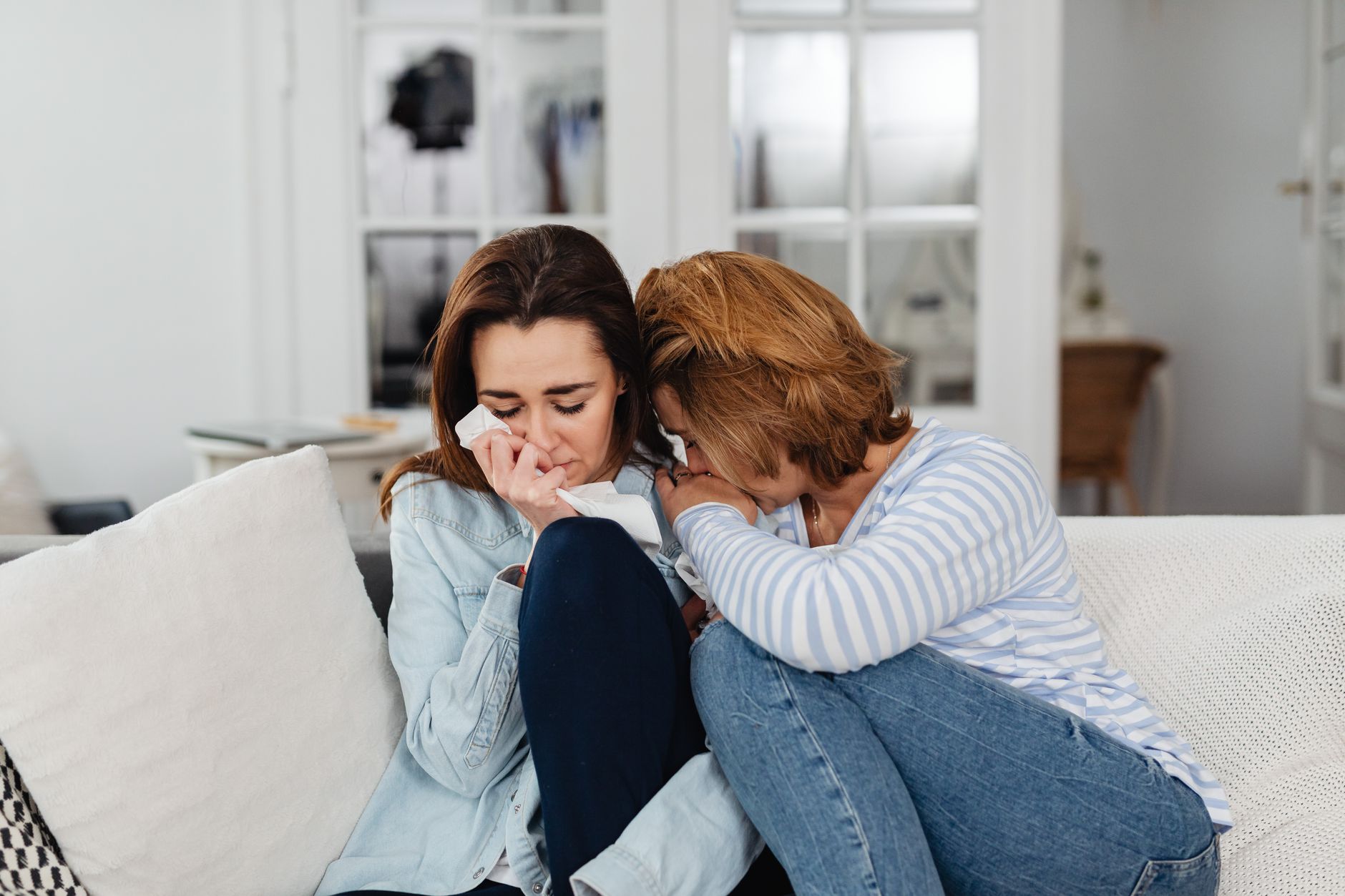 A mom sitting on a couch with her baby, looking exhausted but supported by her partner
