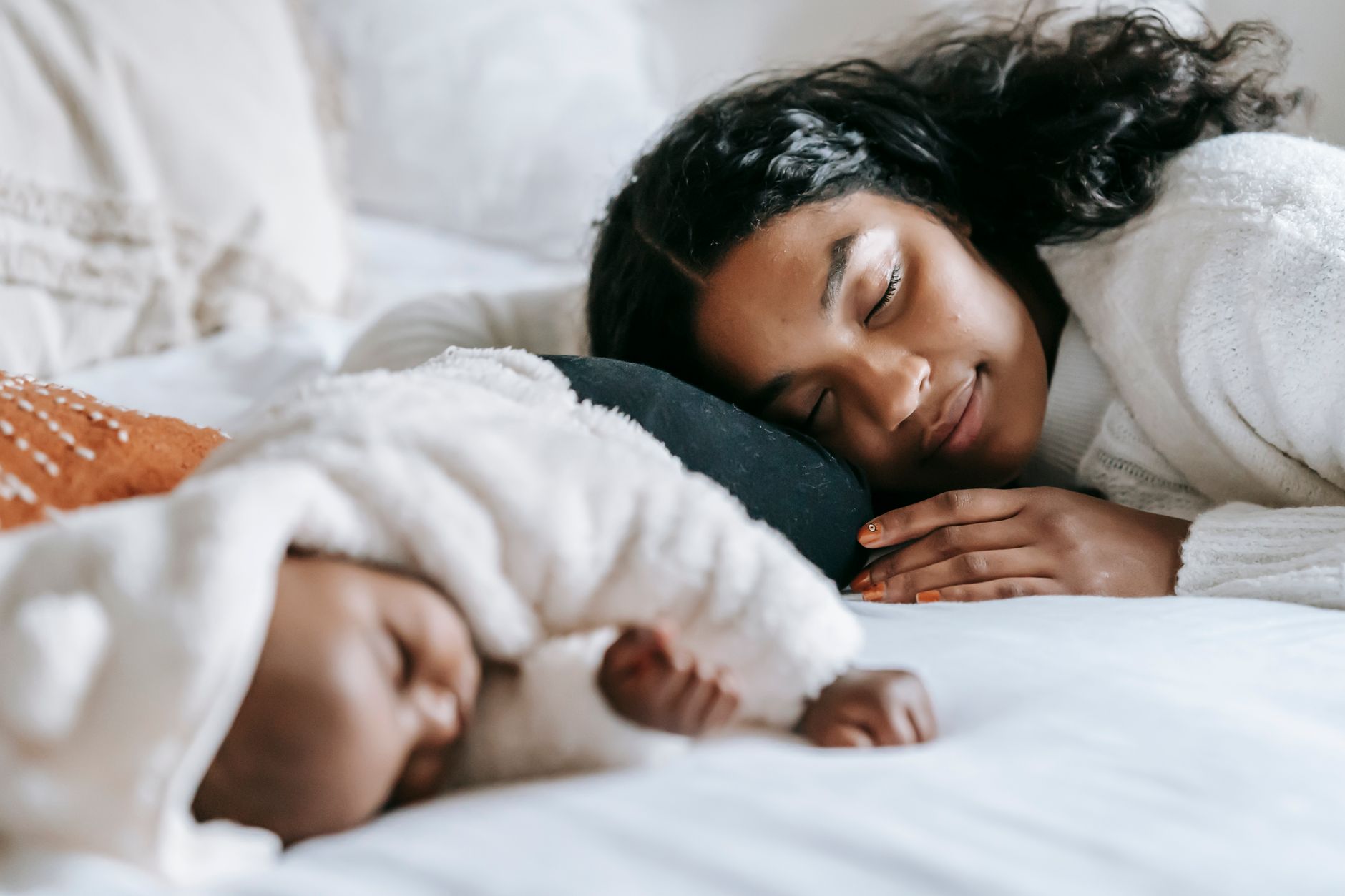 A postpartum mom sitting on a bed with a supportive partner, looking exhausted but content