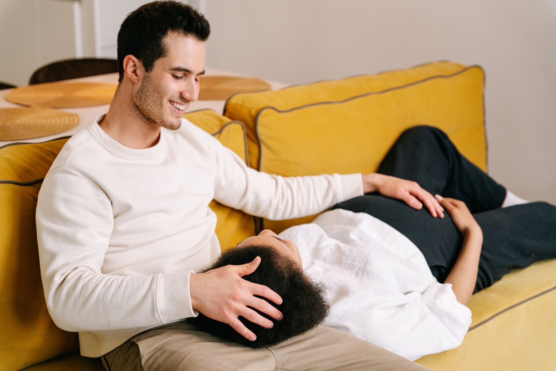 A pregnant woman talking openly with her partner on a cozy sofa, both looking engaged and supportive, in a warm, inviting living room