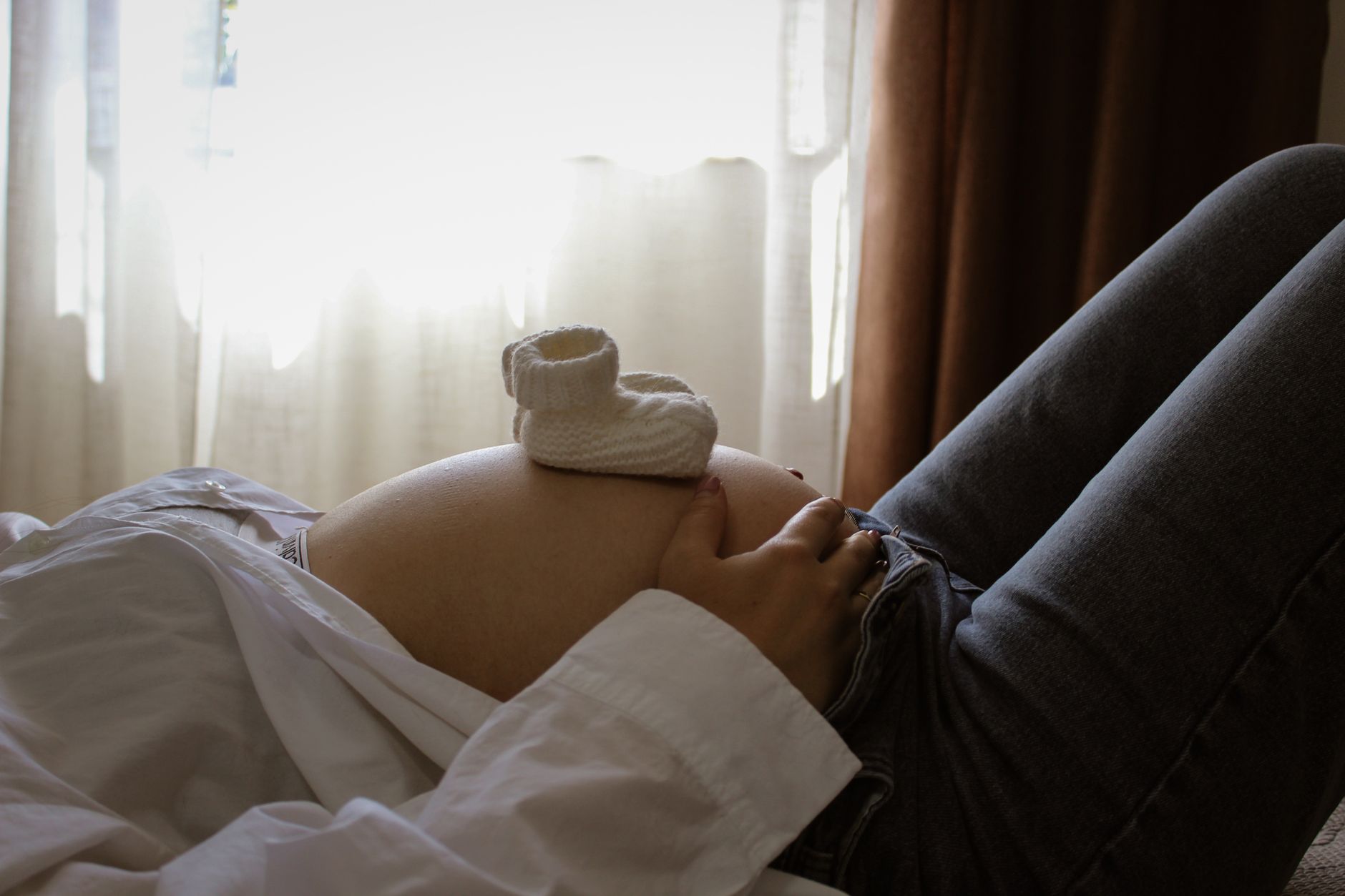 A pair of baby booties, one blue and one pink, resting on a pregnant belly, symbolizing twins
