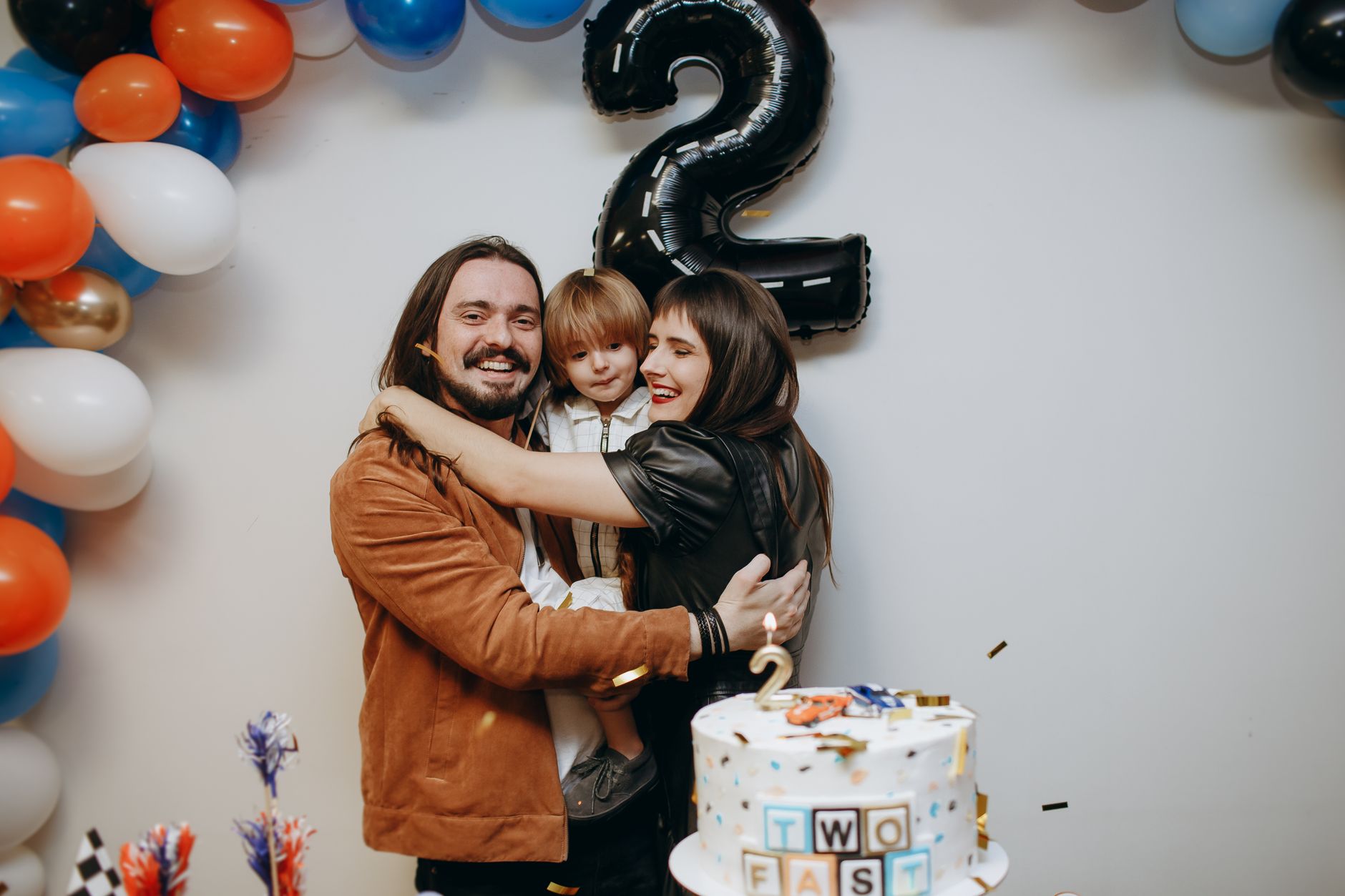 Two parents laughing together with their newborn, surrounded by supportive friends at a baby shower