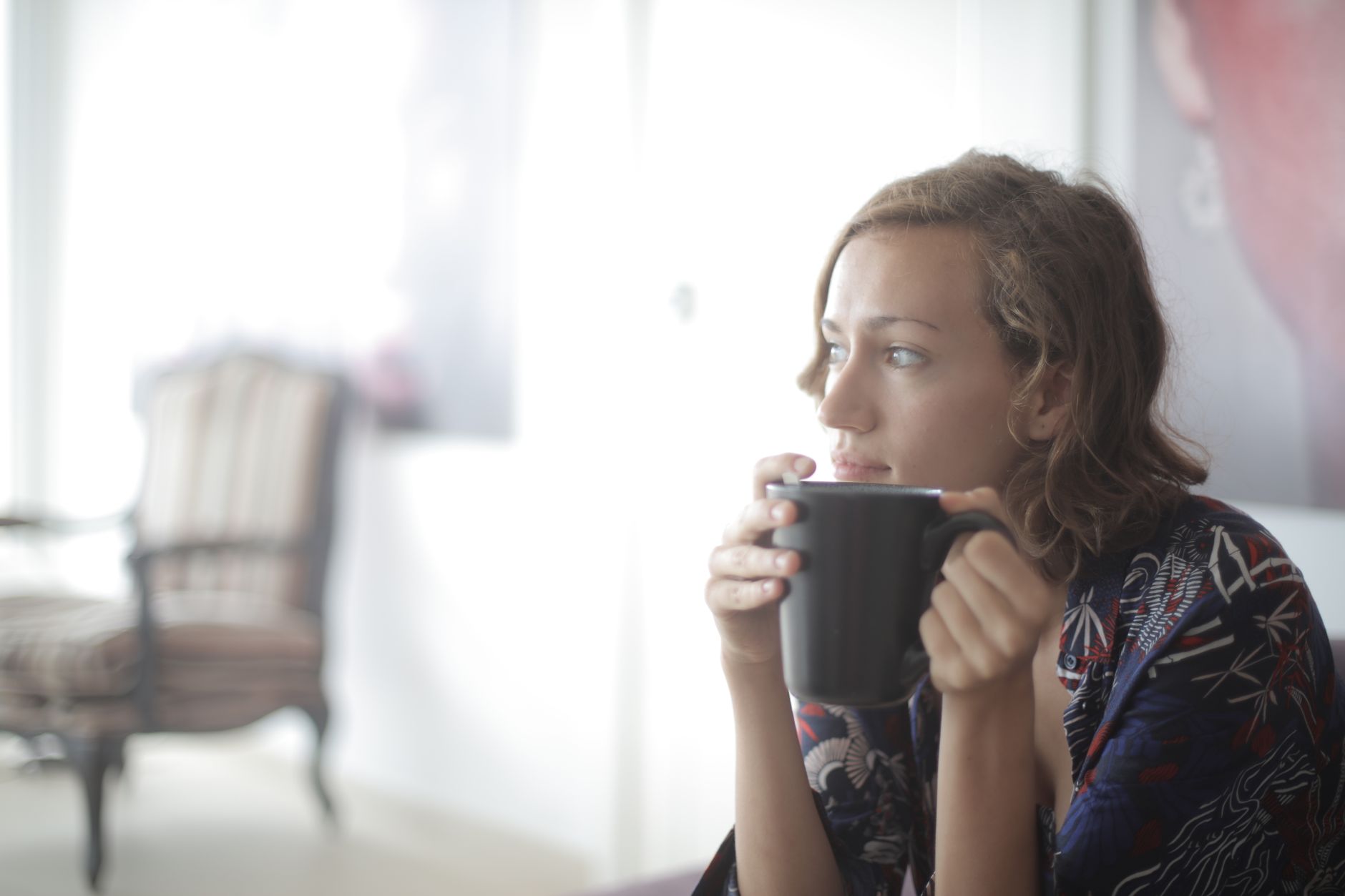 A mom sitting peacefully with a warm cup of tea, looking out a window, capturing a serene moment of self-care amidst the demands of motherhood.