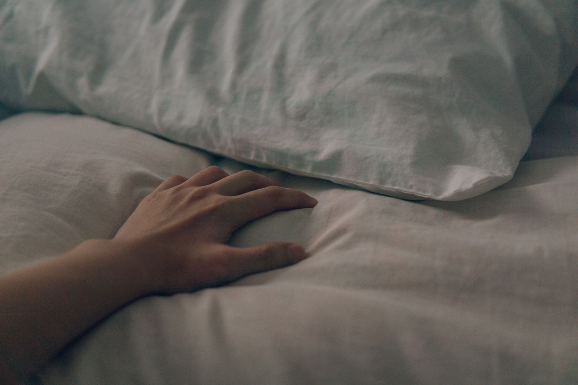 A wedge pregnancy pillow placed under a pregnant woman's belly as she lies on her side, providing targeted support, on a light-colored sheet.