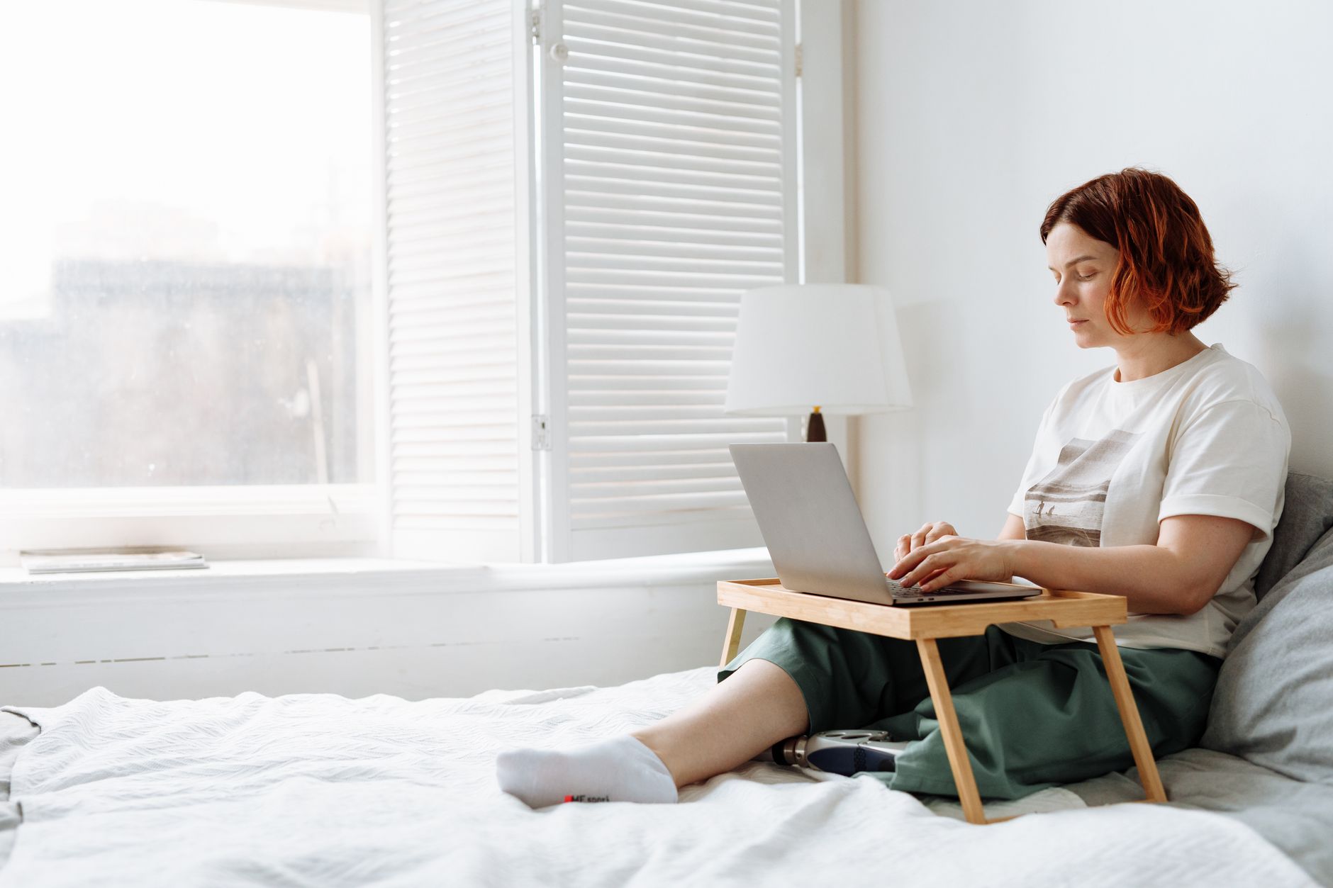 A mom working on a laptop at a kitchen table, surrounded by notebooks and a coffee cup
