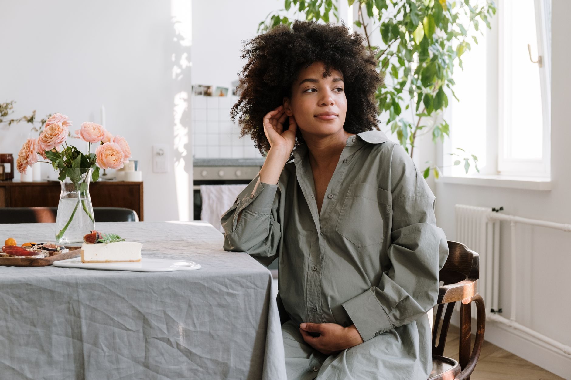A pregnant woman holding a clipboard with her glucose monitoring chart, sitting at a sunny kitchen table with a cup of tea, captured in soft natural light