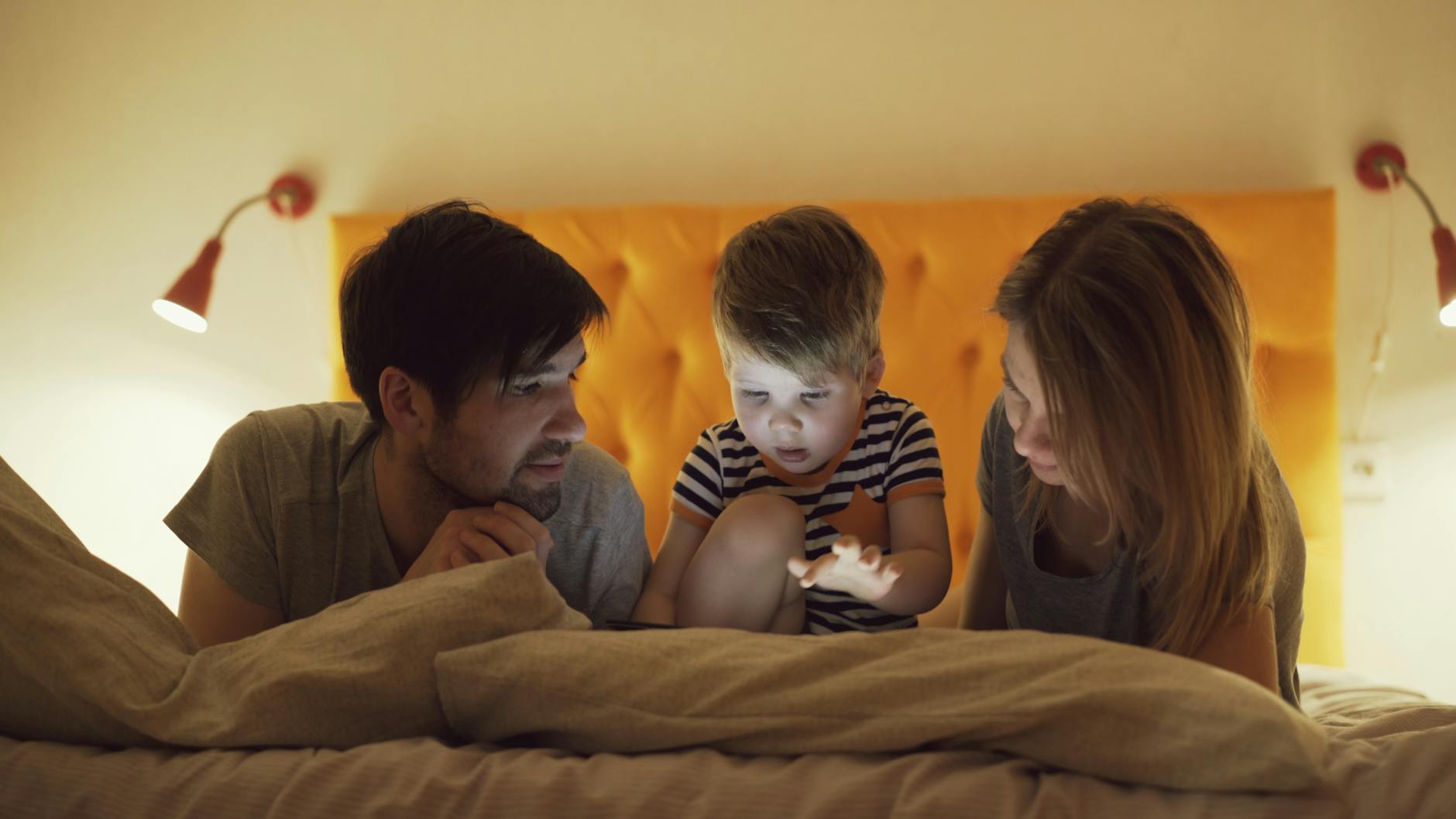 A mother holding a baby on a soft blanket while a digital tablet shows a colorful growth chart, bright morning light, cozy home setting