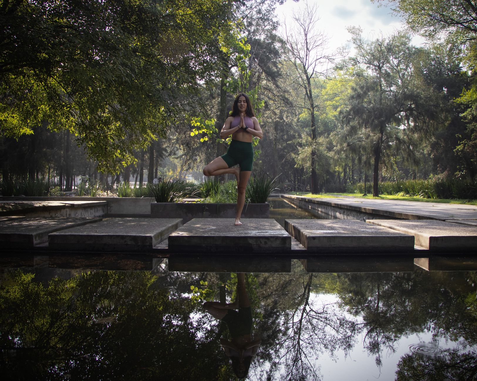 A woman practicing yoga in a serene outdoor setting, surrounded by trees and a lake, warm natural light