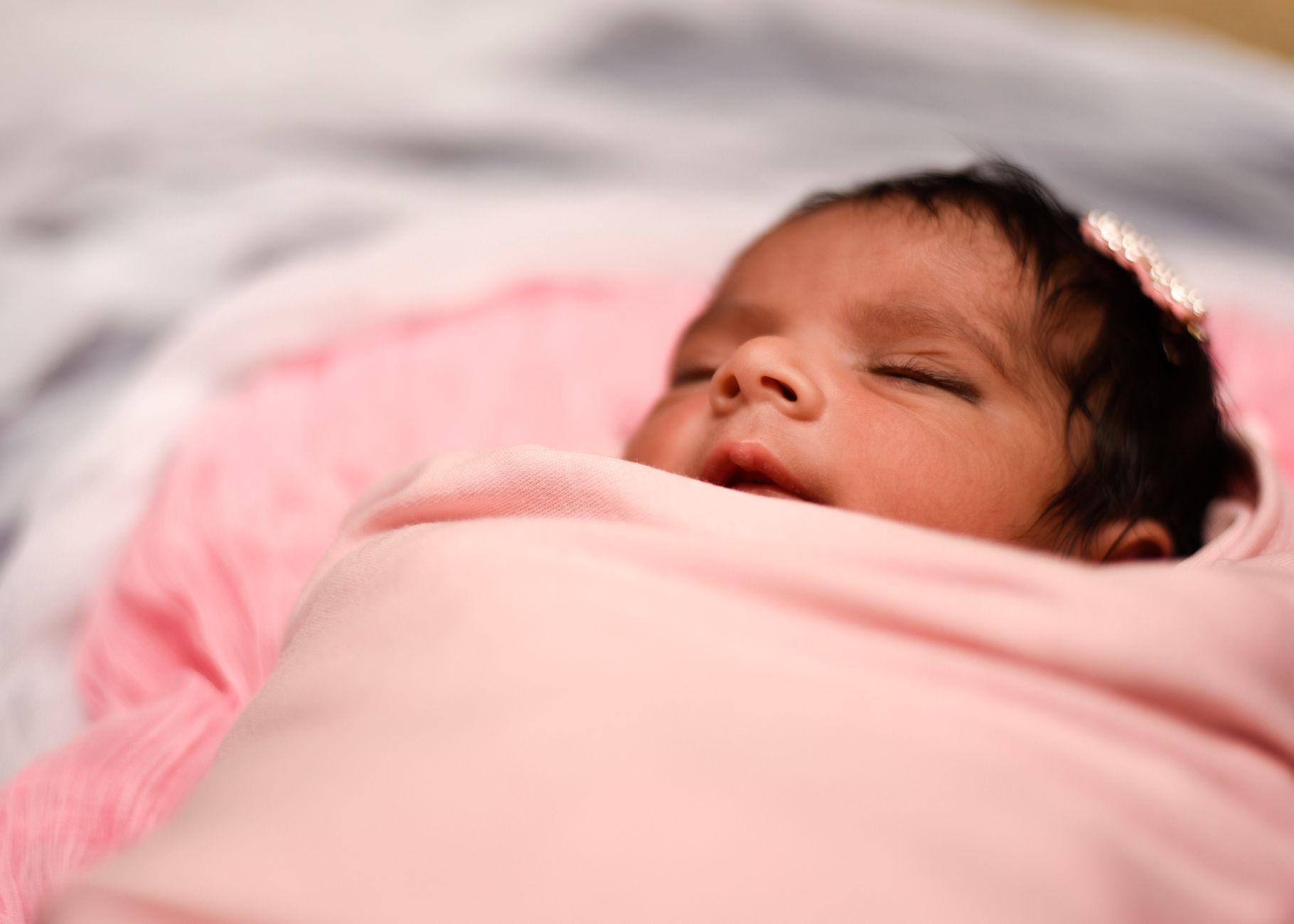 A newborn swaddled in a soft, pastel blanket lying on a windowsill with gentle morning light, highlighting the calm atmosphere of a winter birth