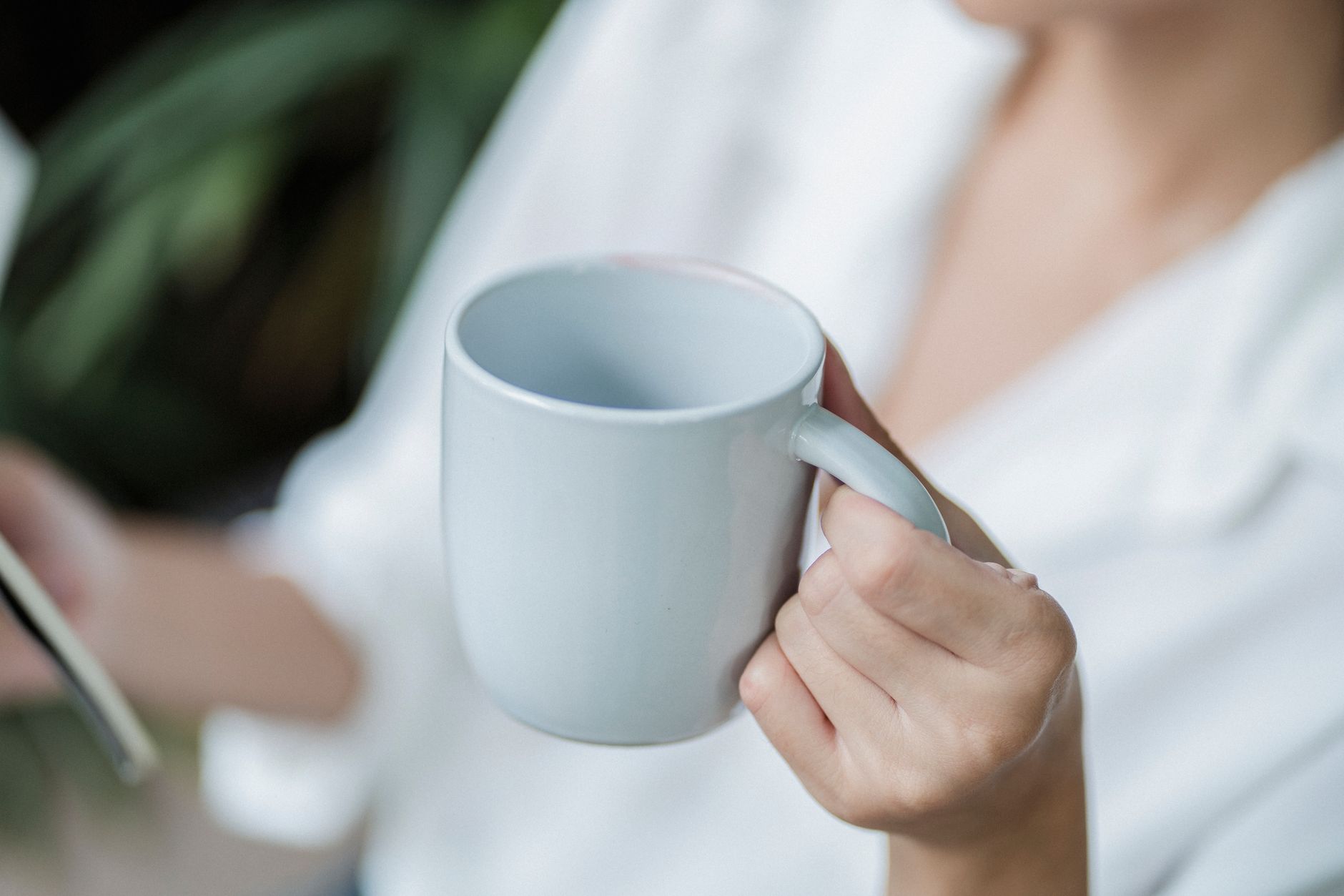 A pregnant woman holding a warm mug of ginger tea while reading a prenatal care guide, illustrating mindful consumption and awareness of safe caffeine limits.