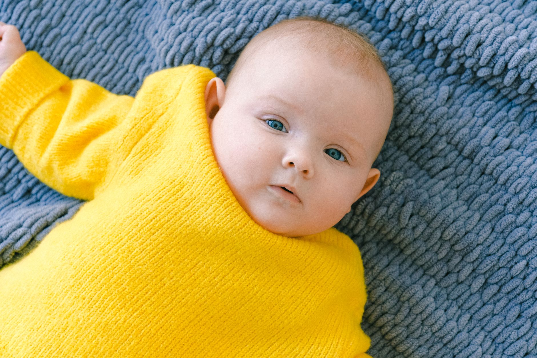 Happy baby on a soft blanket during tummy time, reaching for a bright yellow rattle