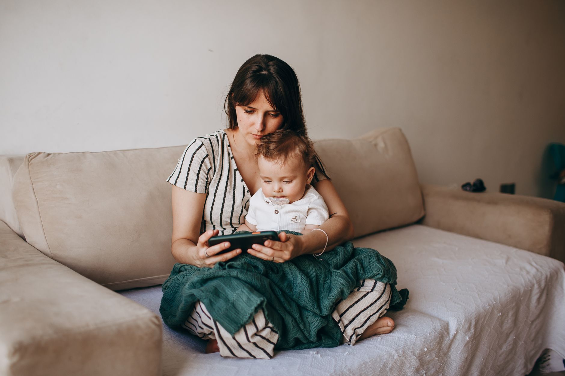 A parent holding a tablet showing a simple animated book while a five‑month‑old baby looks on, soft natural light from a nearby window