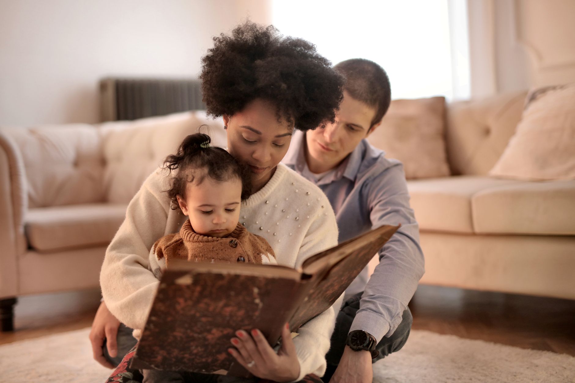 A parent sitting on a soft rug reading a colorful board book to a curious seven-month-old baby, natural light streaming through a window