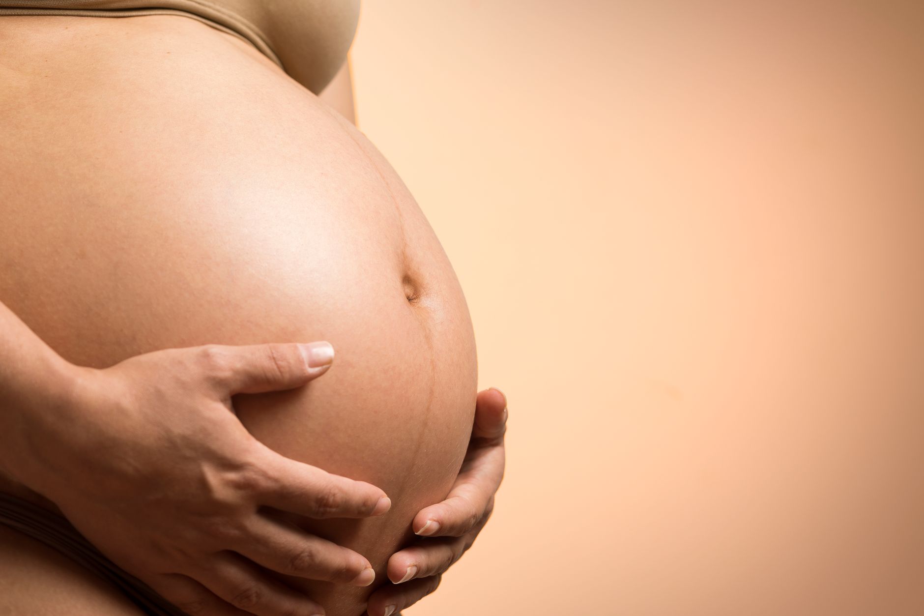 A woman gently applying pregnancy-safe body oil to her belly with soft, circular motions, cozy bedroom setting, natural light