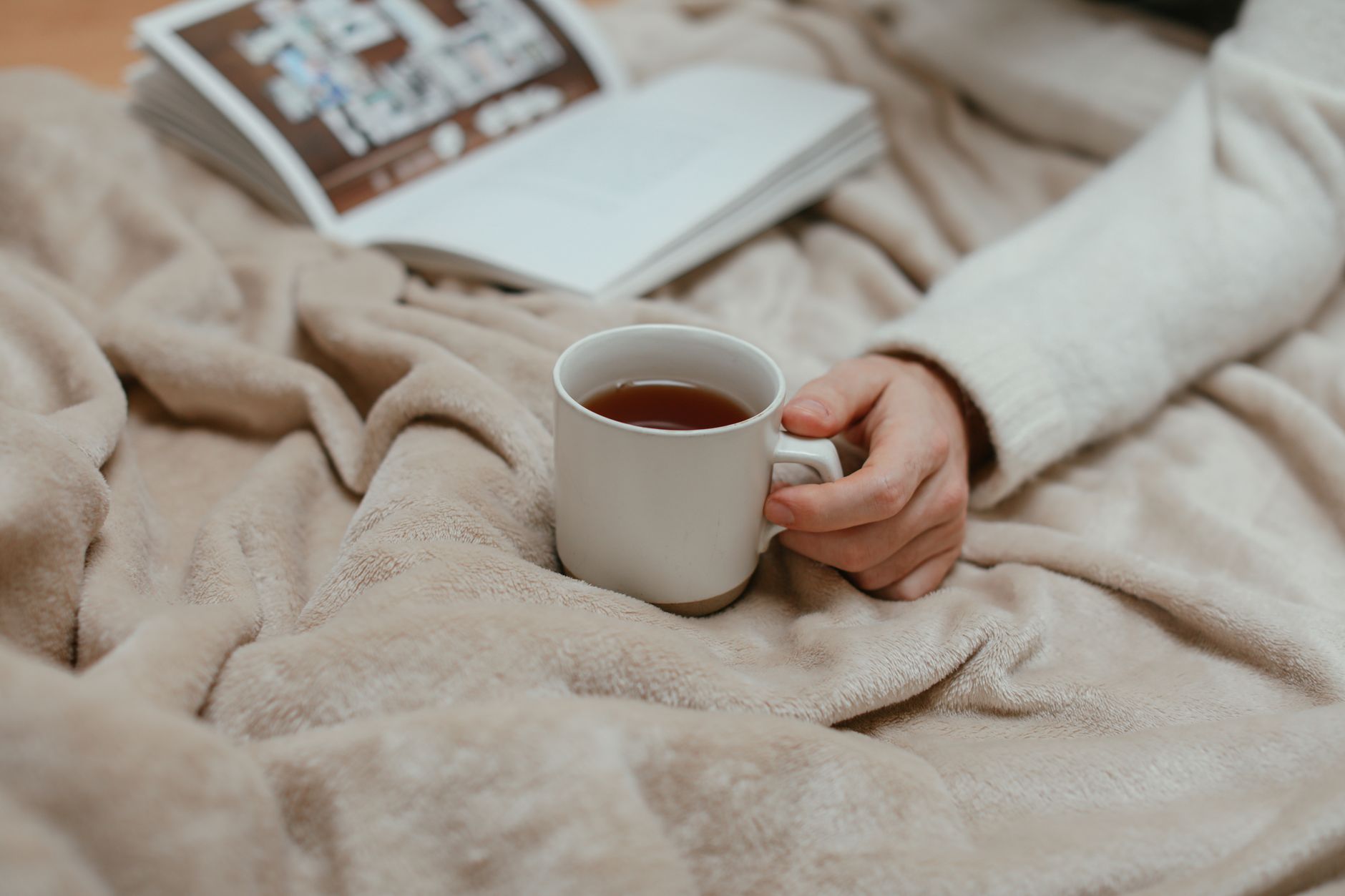 Pregnant woman resting on a couch with a soft blanket, holding a warm cup of tea while looking at a phone, soft natural light highlighting her belly
