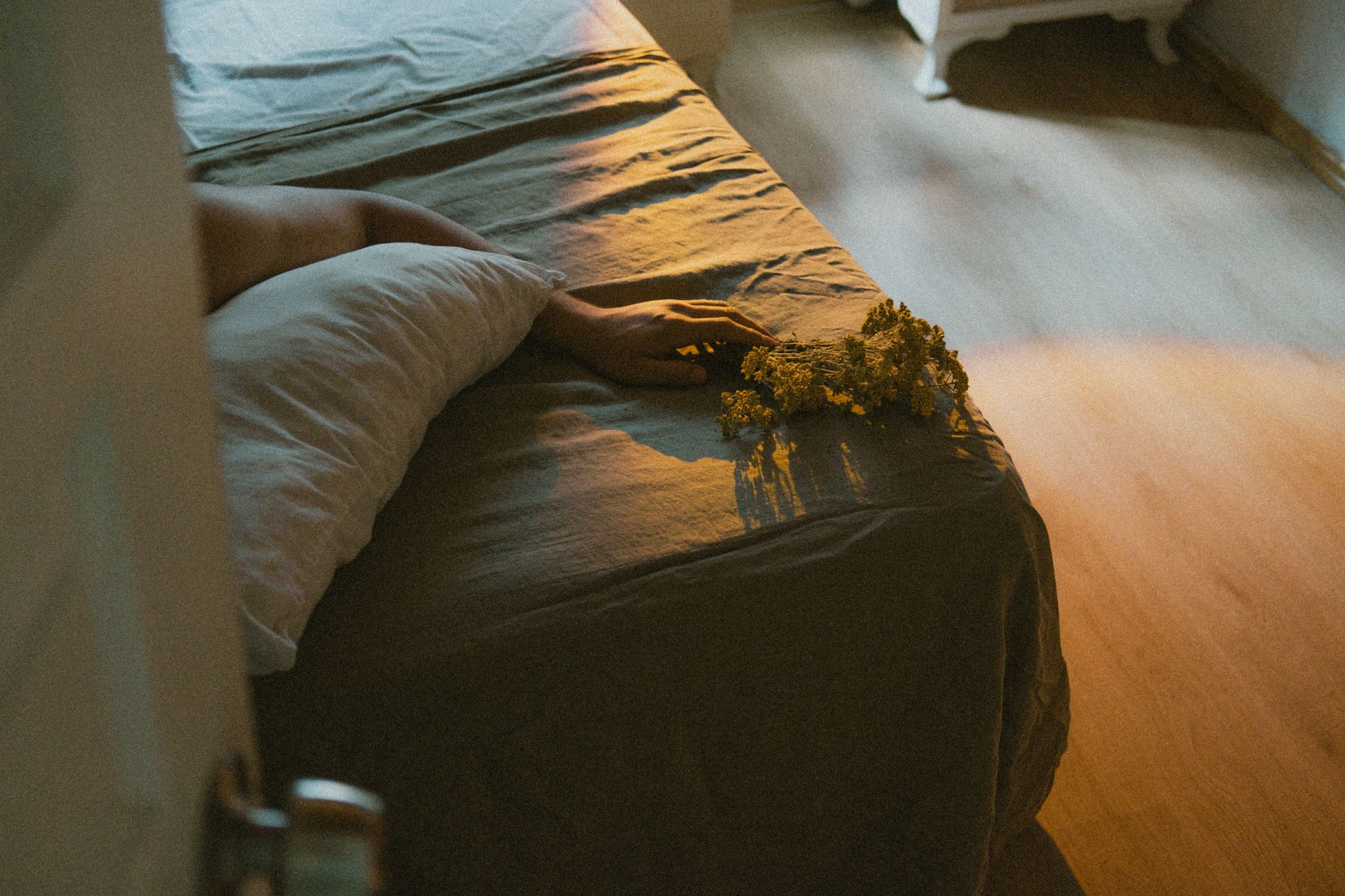 A set of pregnancy pillows on a bedroom floor: a full‑length body pillow, a wedge pillow, and a small knee pillow, arranged on soft linen, bright natural light