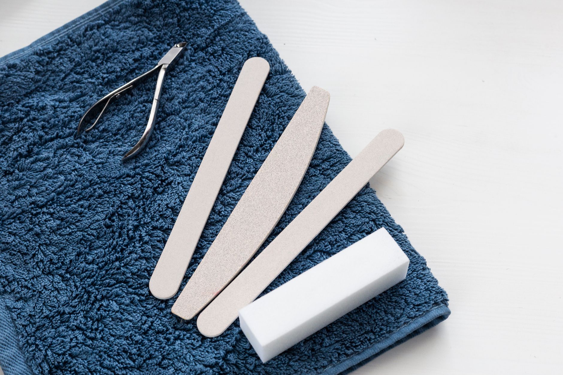 a set of baby nail care tools on a soft pastel blanket, including safety-guard clippers, rounded-tip scissors, and a gentle electric nail grinder, arranged for easy access