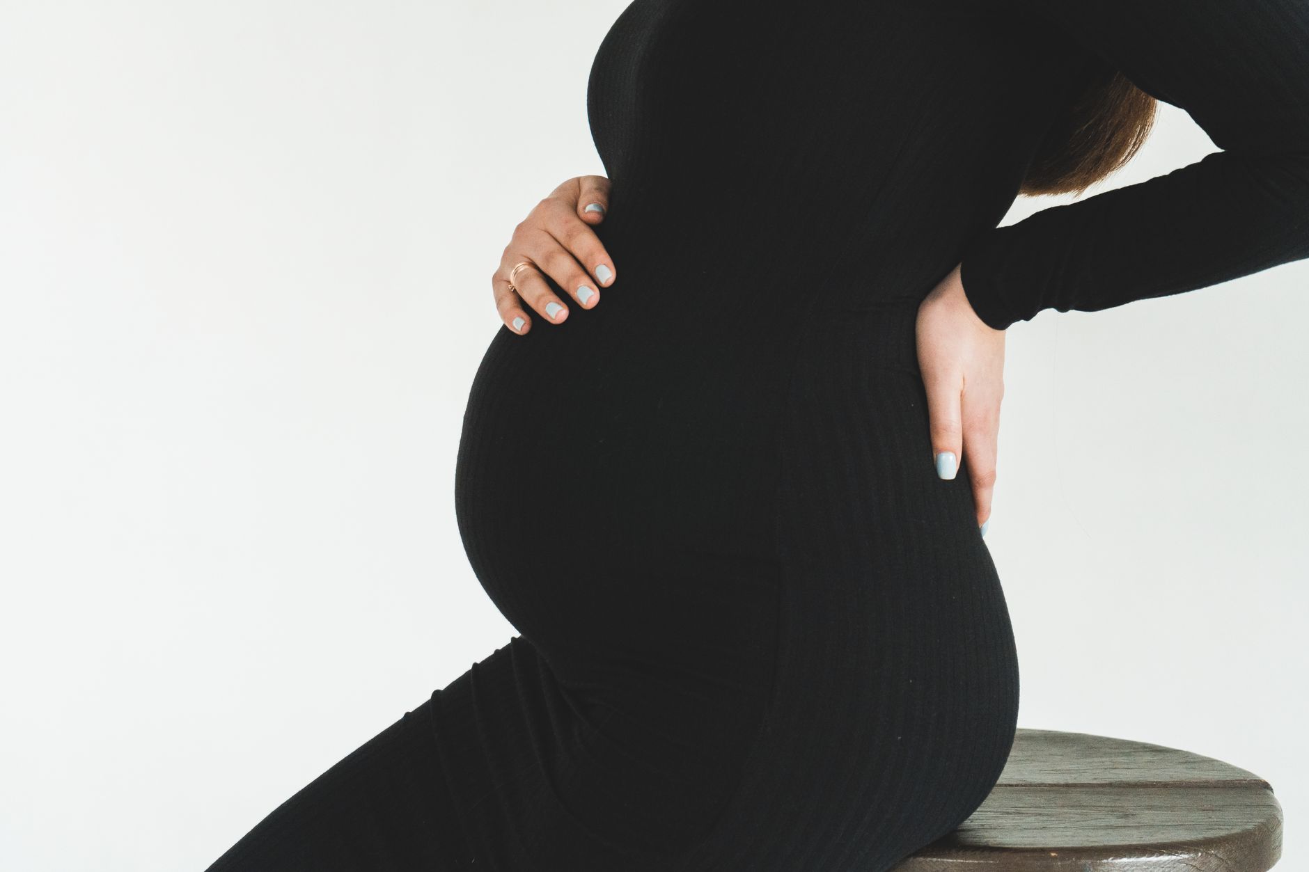 Pregnant woman sitting upright at a desk with a lumbar pillow, natural light streaming through a window, calm workspace