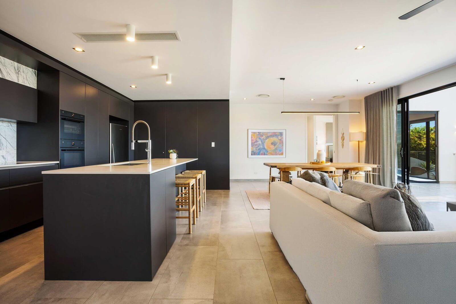Open-plan living and kitchen area featuring dark matte cabinetry, a white stone island, and a dining space.